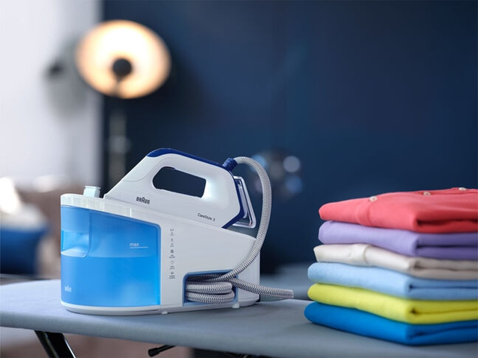 Ein Dampfbügeleisen und Kleidung. Das Eisen ist blau und weiß. Kleidung ist bunt.