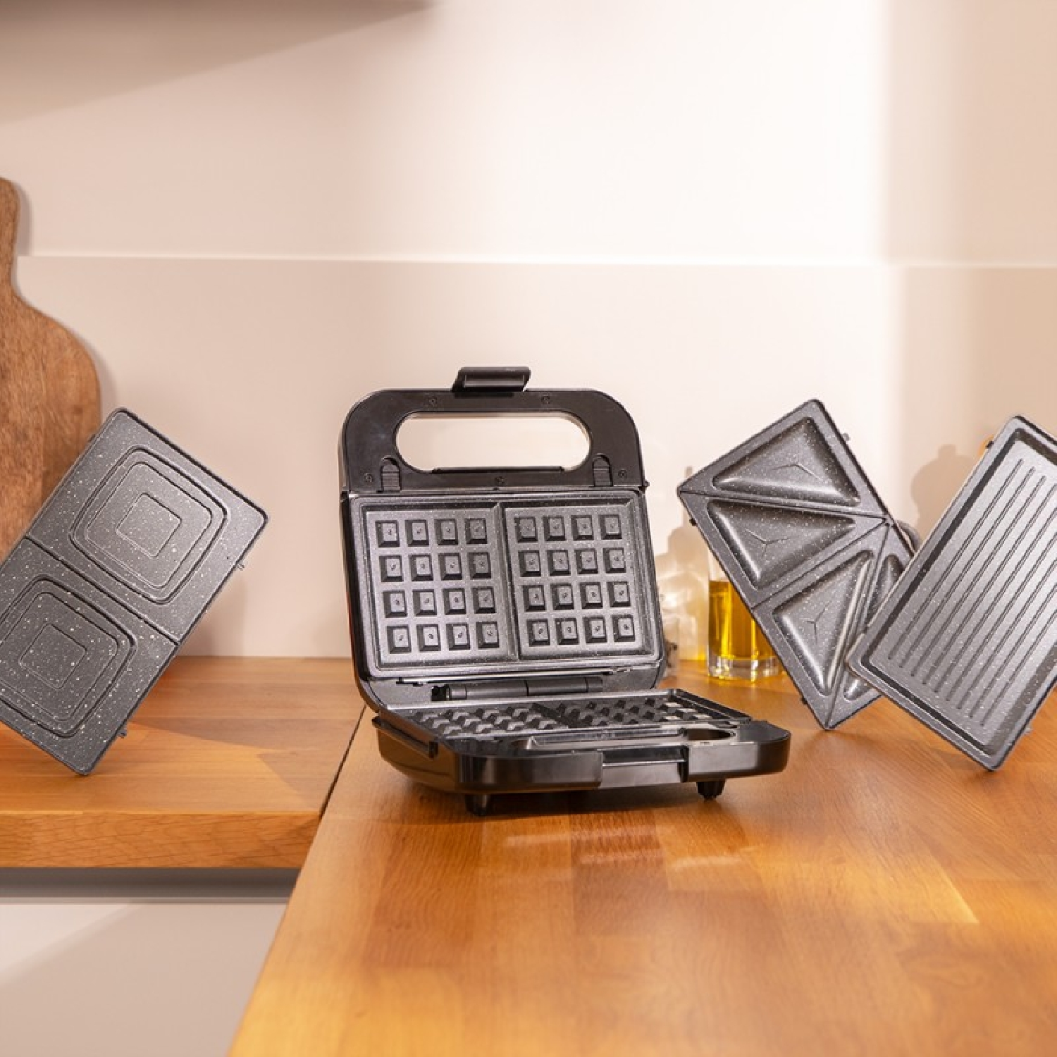Zwarte wafelmaker, open, met twee platen en twee losse platen op een houten oppervlak.