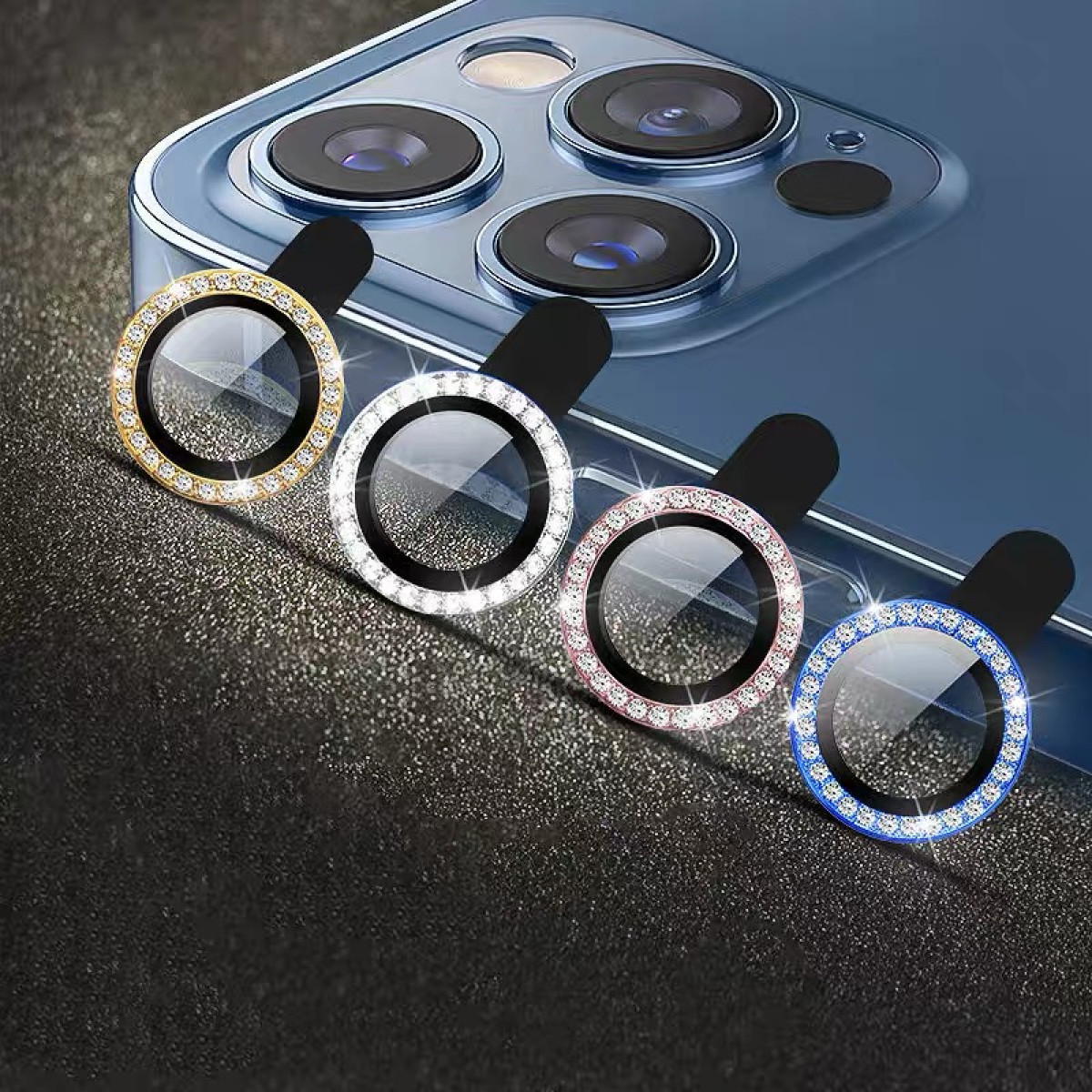 Vier kleurrijke telefoonlensbeschermers met strass, geplaatst op de camera van een blauwe telefoon.