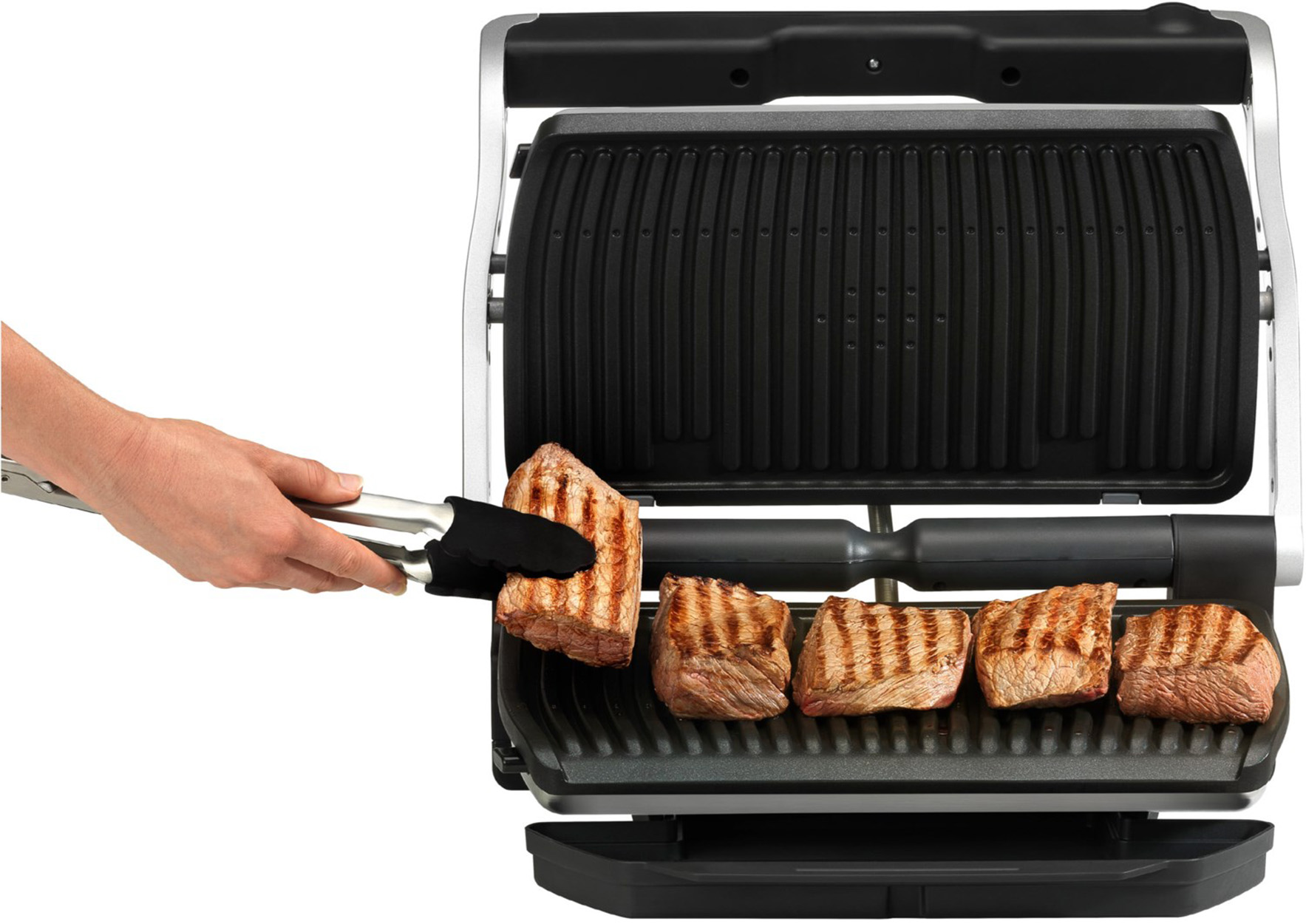 Eine Hand verwendet eine Zange, um ein gegrilltes Steak auf einen Grill zu legen. Mehrere Steaks sind bereits auf dem Grill.