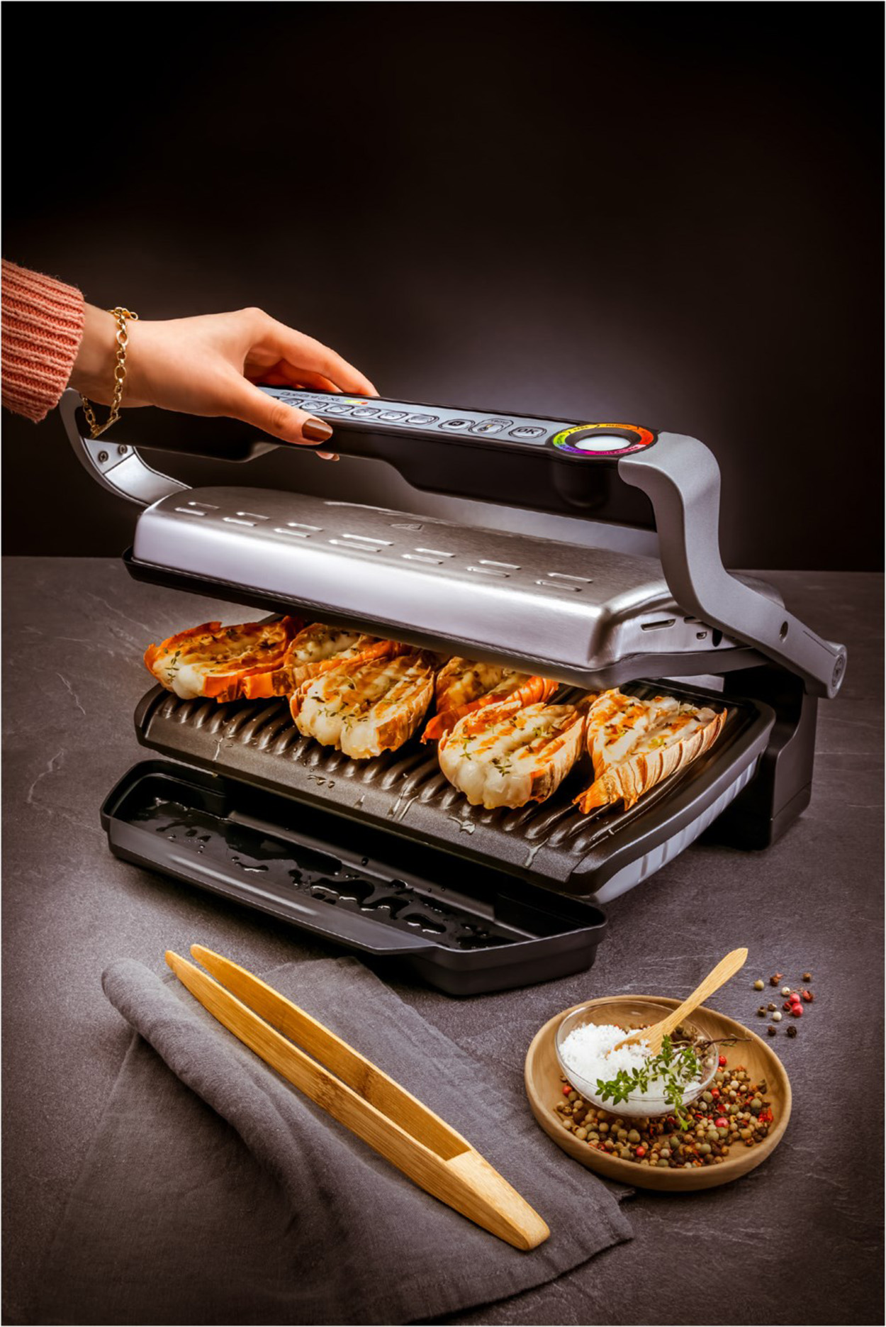 Gegrilltes Essen auf einem Grill, mit Zangen, Salz und Pfeffer, auf dunklem Hintergrund.
