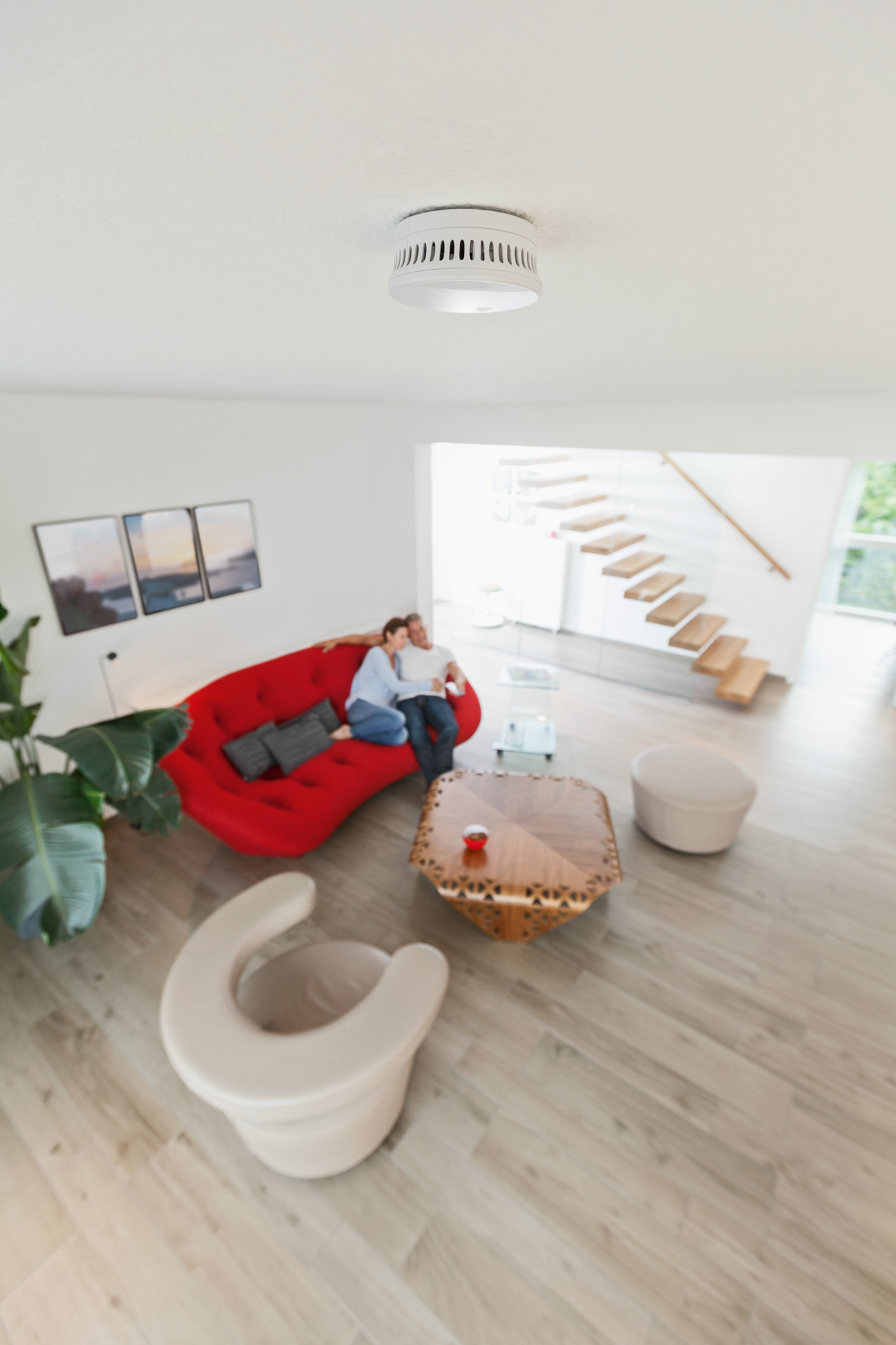 Paar auf rotem Sofa, Rauchmelder an der Decke. Modernes Wohnzimmer.
