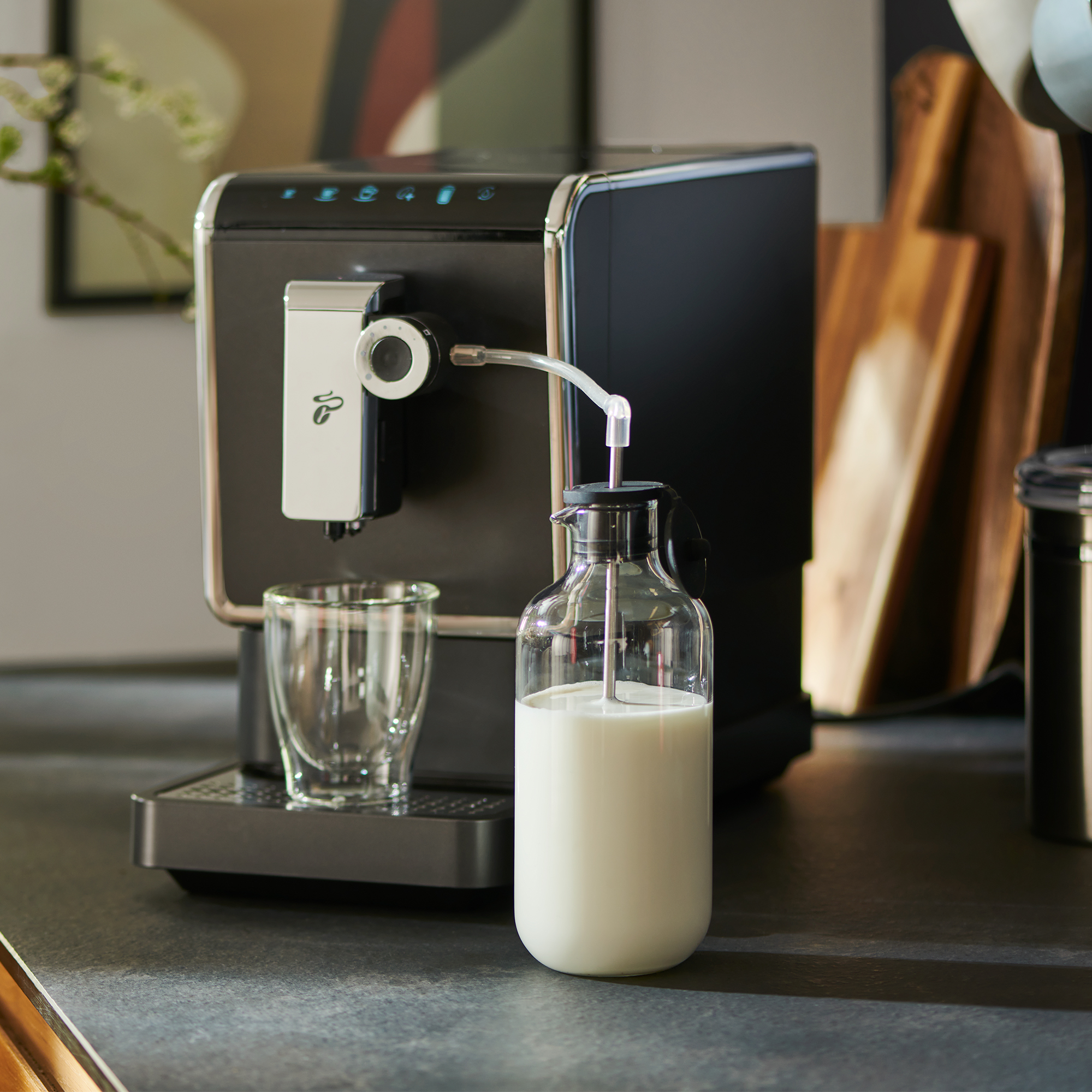 Espressomaschine mit Milchaufschäumer. Milchflasche mit angeschlossenem Schlauch, Glas und Holzschneidebretter.