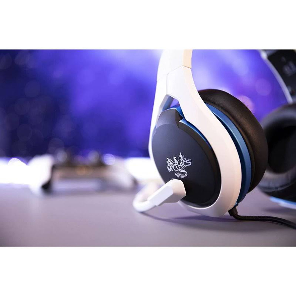 Weiß-schwarzes Gaming-Headset mit blauen Akzenten. Es liegt auf einer grauen Oberfläche mit unscharfem Hintergrund.