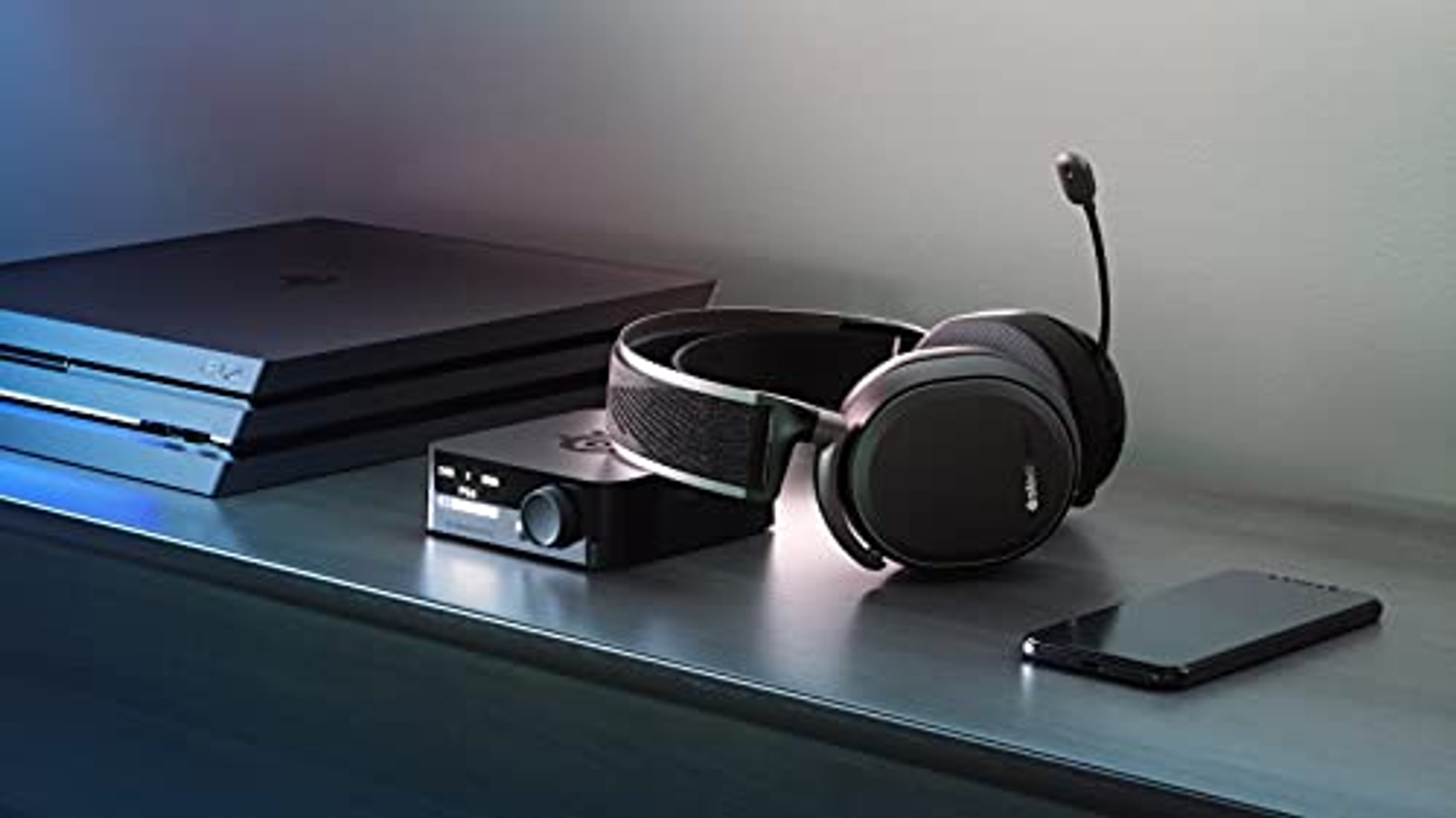 Una configuración de juego con auriculares, una caja de control, una consola PS4 y un teléfono inteligente.