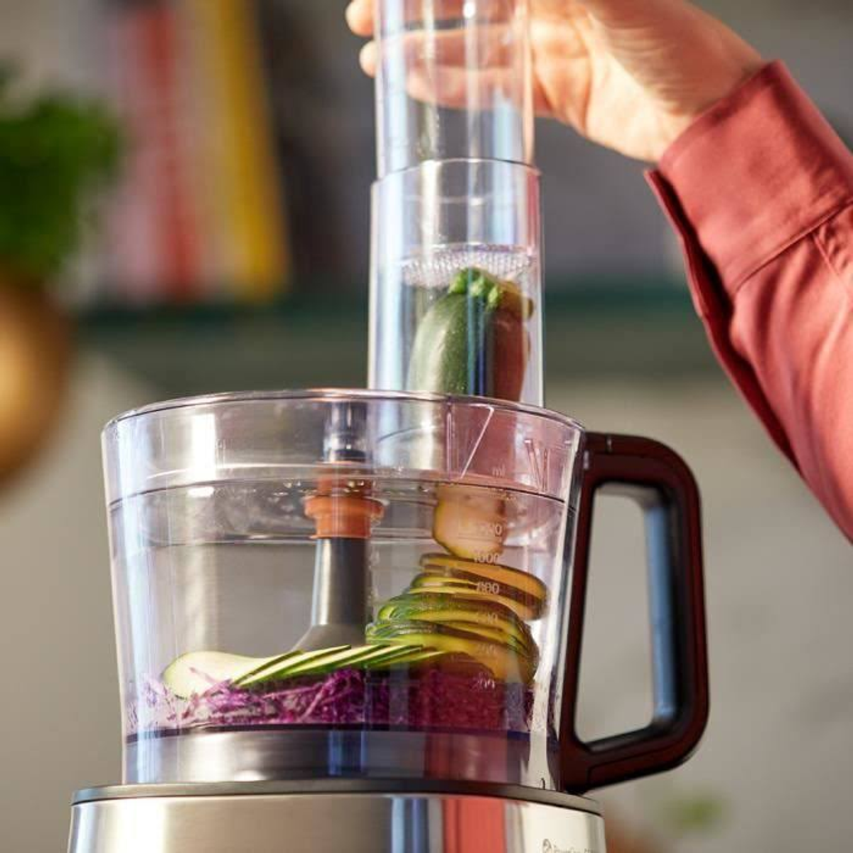 Robot da cucina con verdure. Mano che aggiunge verdura sopra.