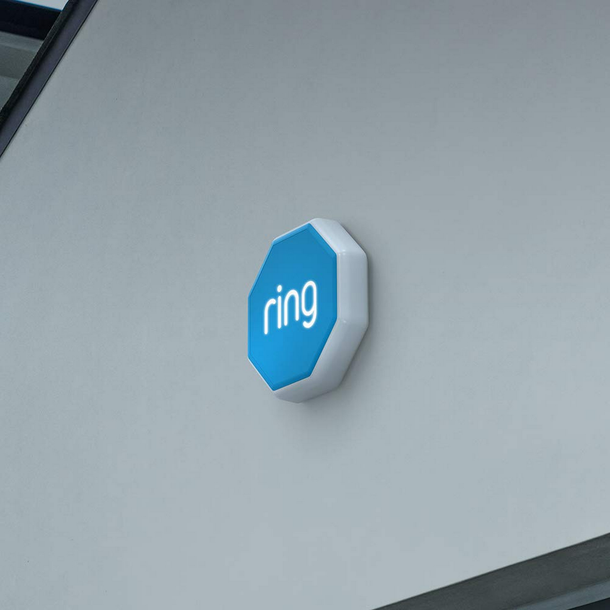Dispositivo de seguridad Ring blanco montado en una pared gris claro. El logo de Ring es azul.