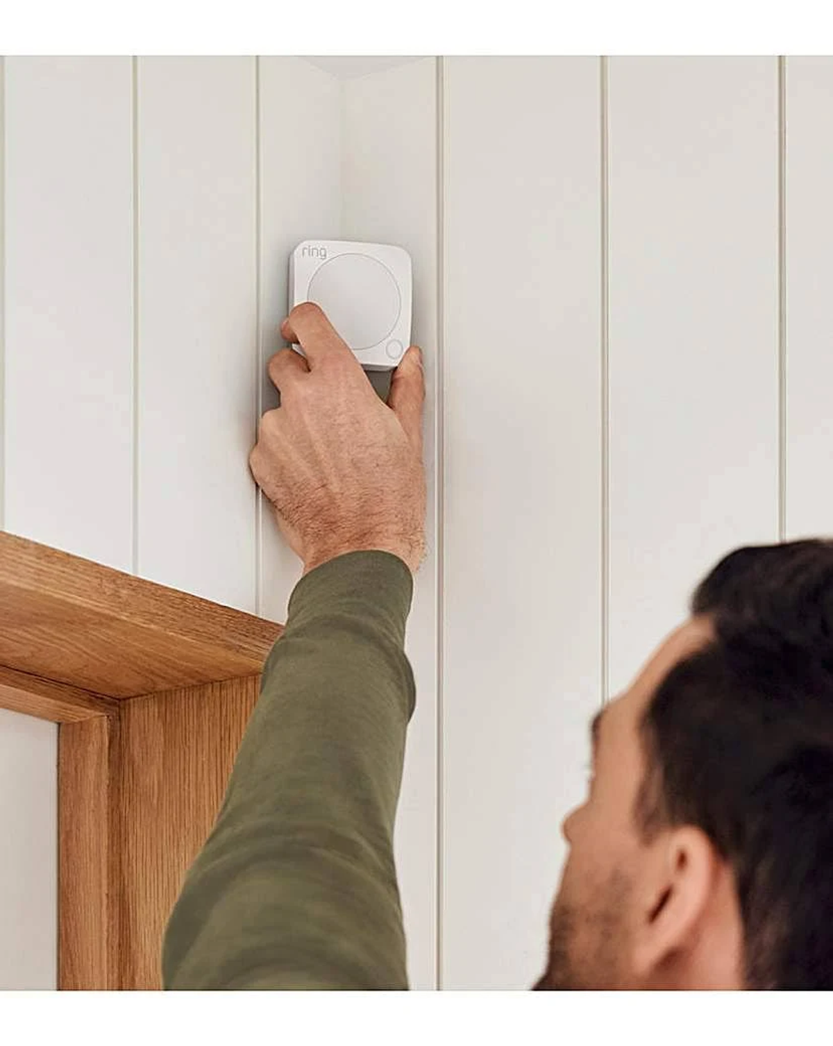 Una mano coloca un dispositivo inteligente cuadrado blanco en una pared con paneles blancos.