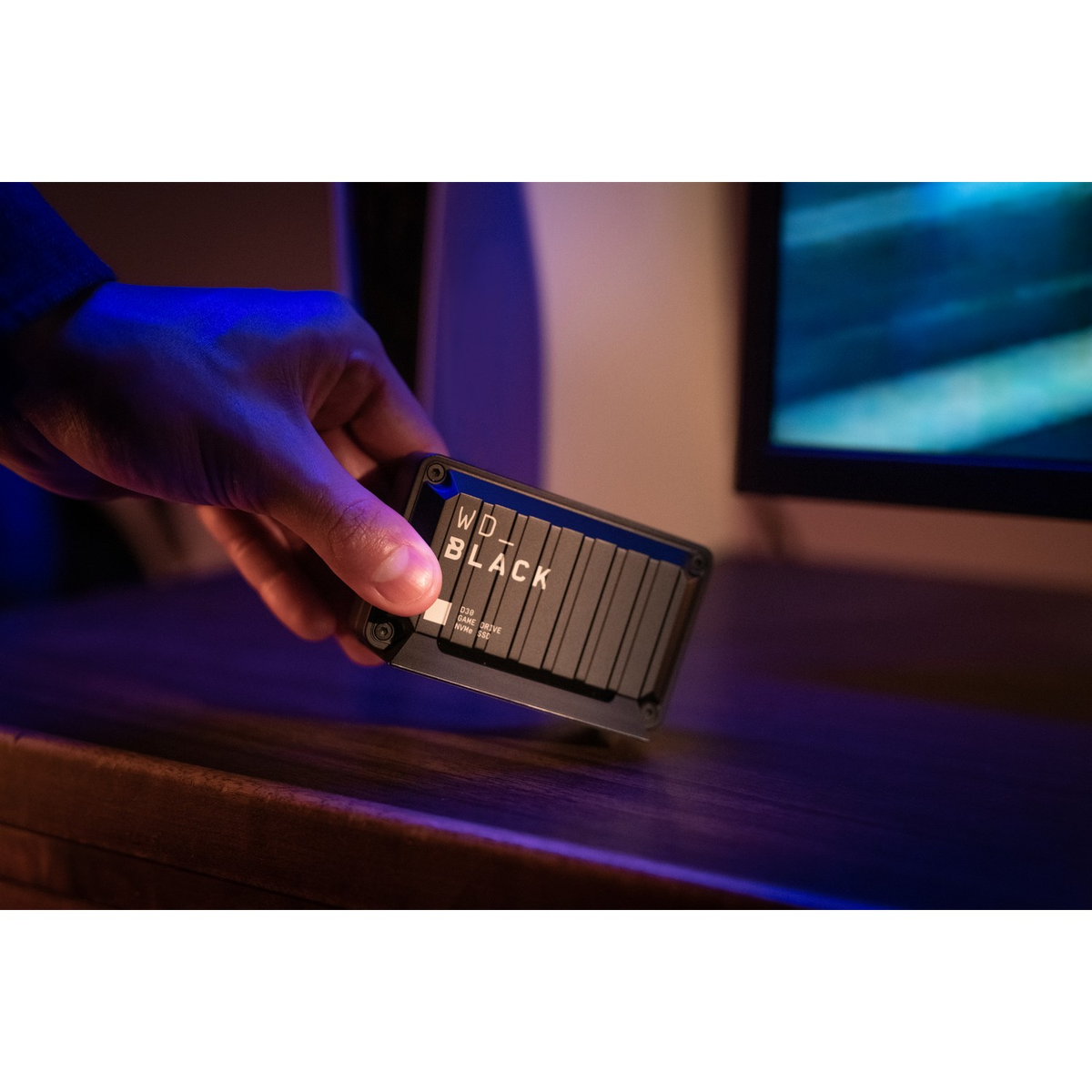 Ręka trzymająca czarny zewnętrzny dysk twardy WD Black. Ekran komputera w tle.