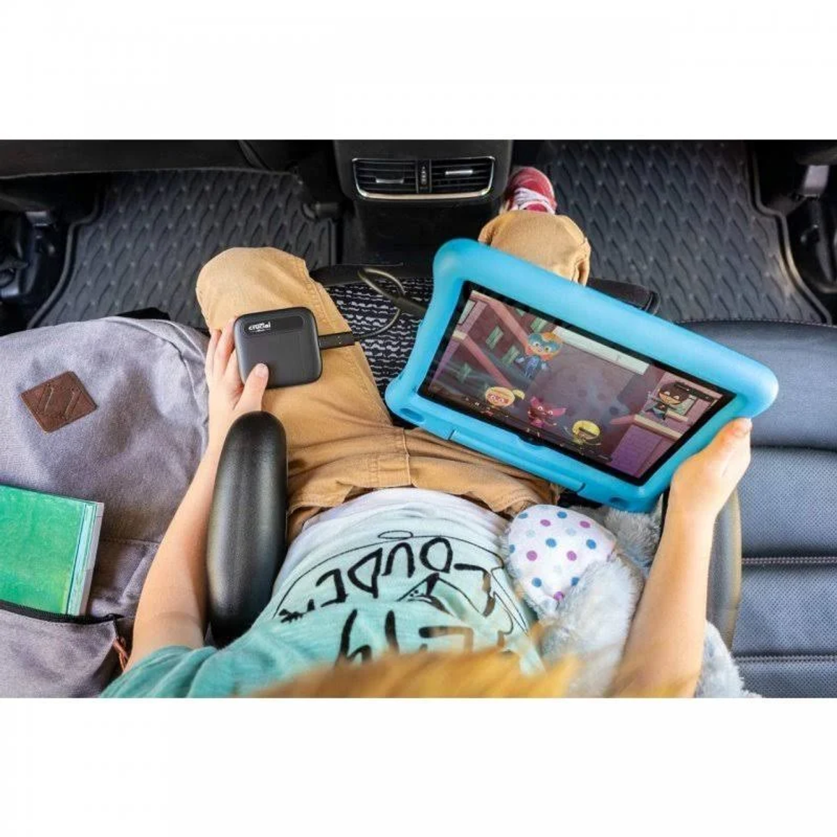 Dziecko w samochodzie, gra w grę na niebieskim tablecie, podłączone do czarnego urządzenia ładującego.