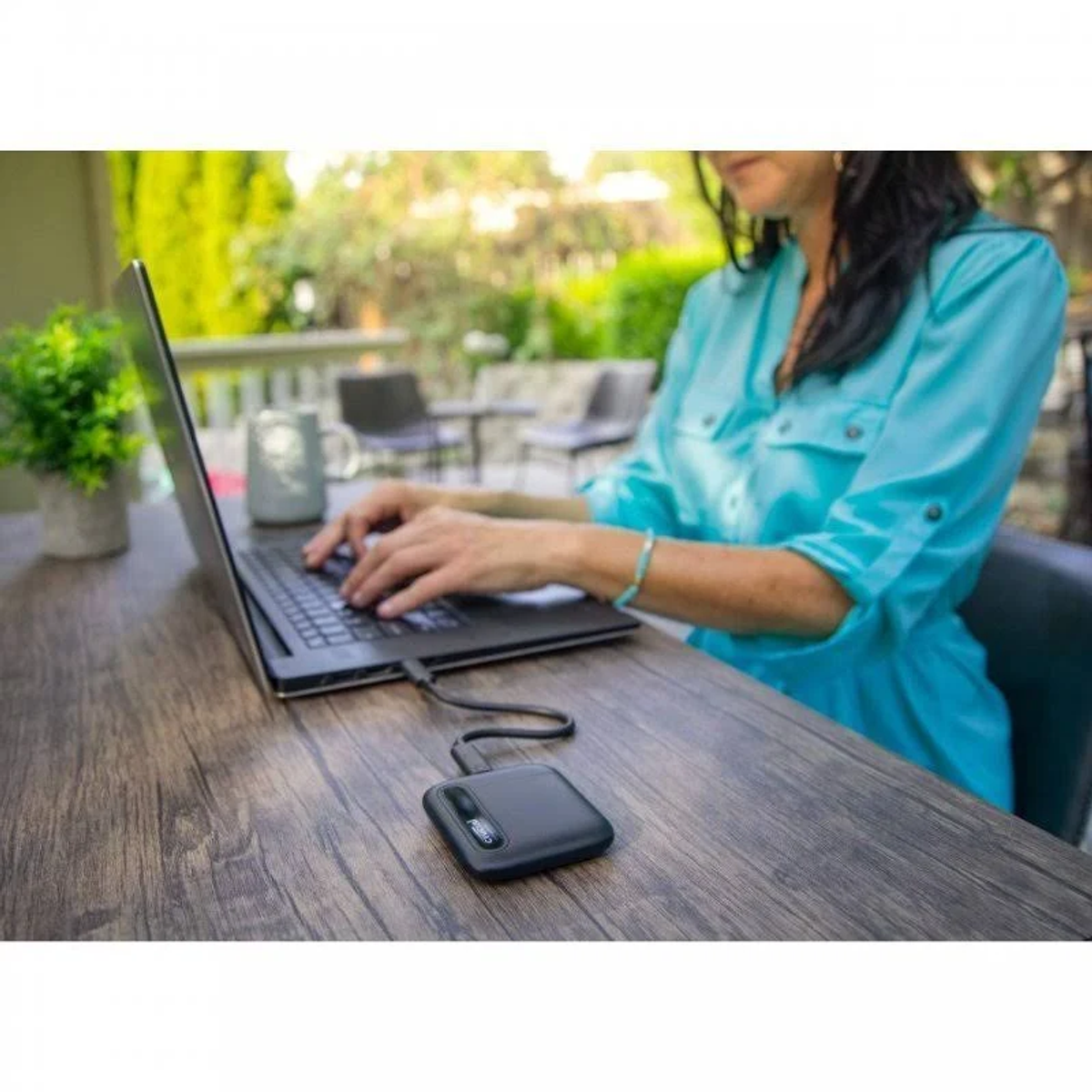 Kobieta używająca laptopa na drewnianym stole z podłączonym przenośnym dyskiem twardym.