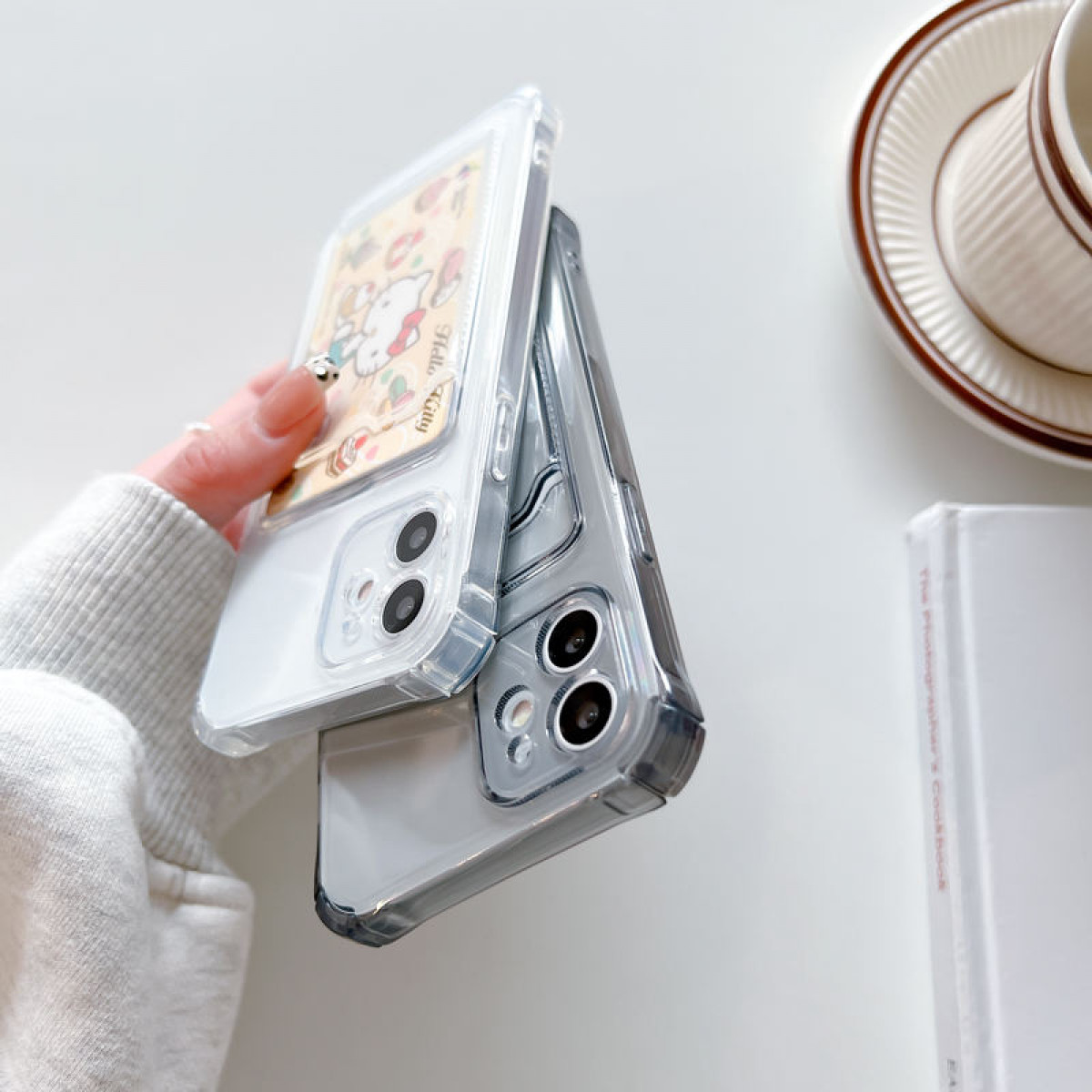 Zwei Telefonhüllen gehalten. Eine ist weiß mit Hello Kitty-Design, die andere grau.