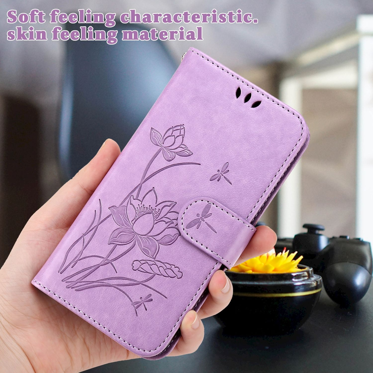 Hand hält eine lila Handyhülle mit Lotus- und Libellenmuster, in der Nähe einer gelben Blume.