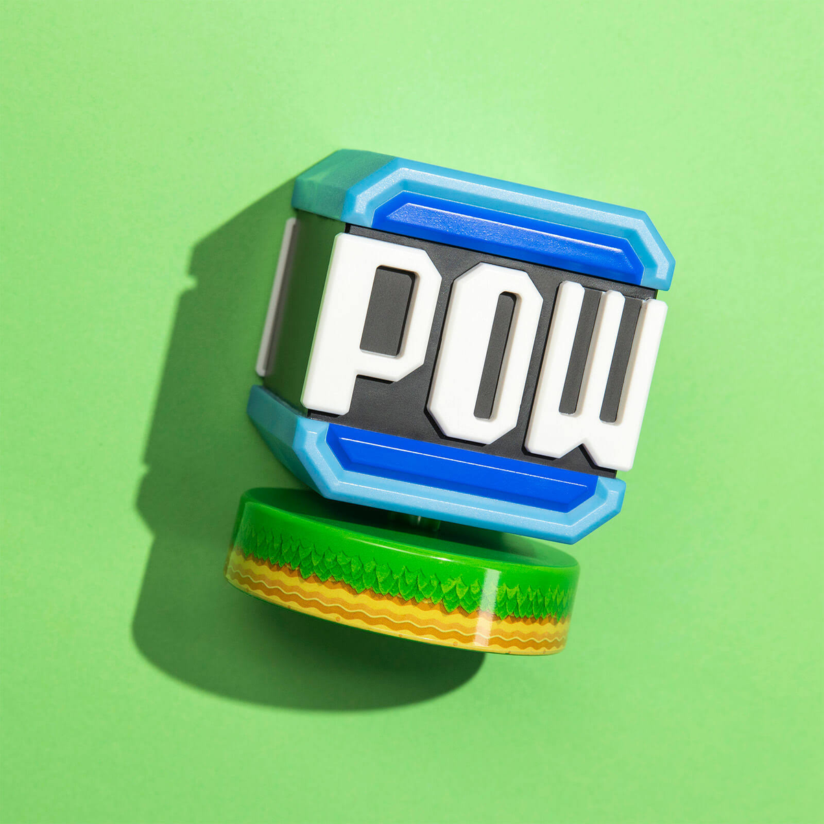 POW Würfel Spielzeug auf Grün. Blaue, weiße und grüne Farben. Grüne Basis mit gelbem Streifen.