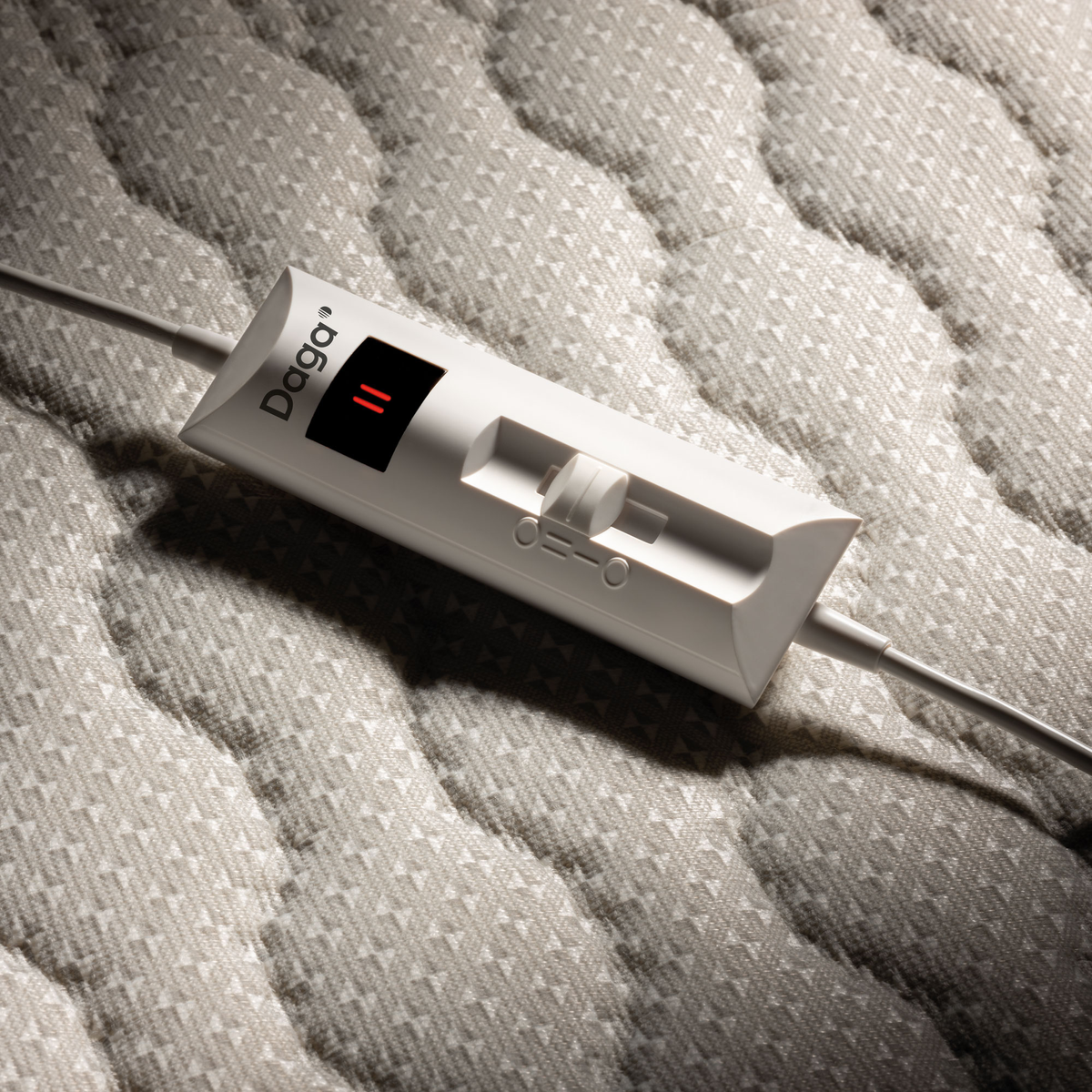Control de manta eléctrica blanco con dial y pantalla roja iluminada, sobre tela gris.