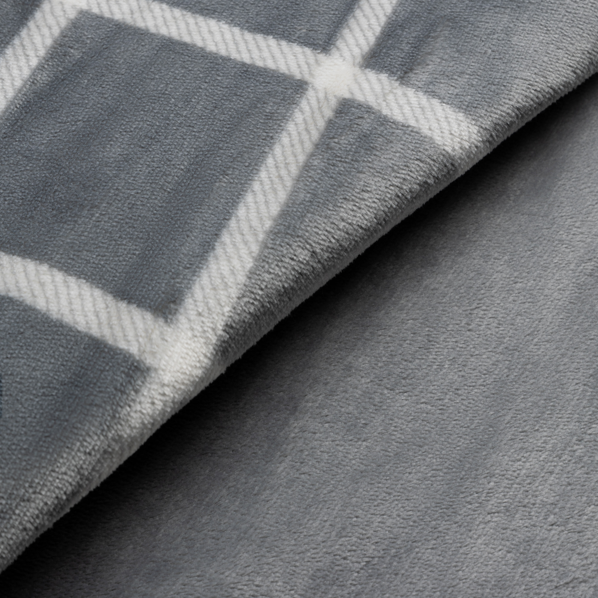 Zbliżenie na szary koc z białym wzorem w romby, miękką fakturą i złożoną krawędzią.