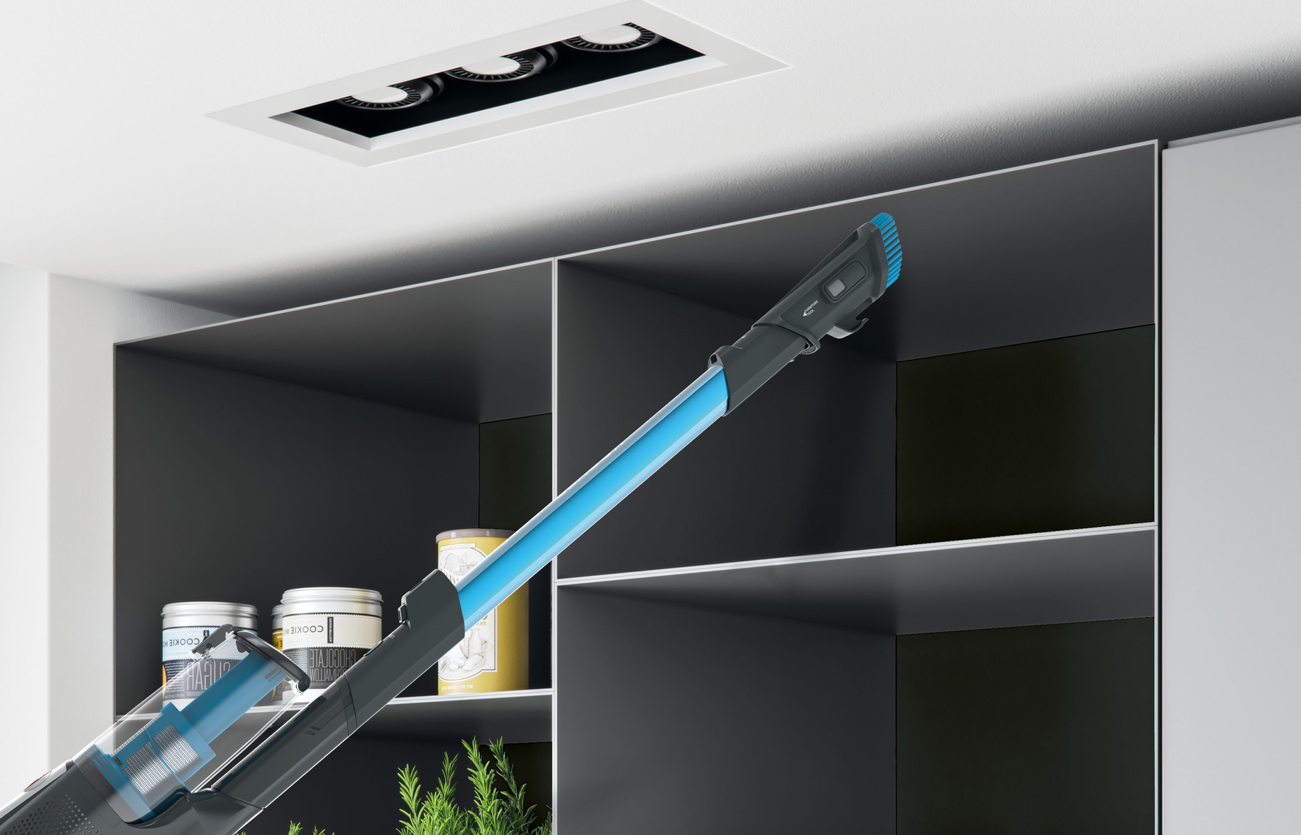 Una aspiradora con una extensión azul limpiando una estantería en una cocina moderna.