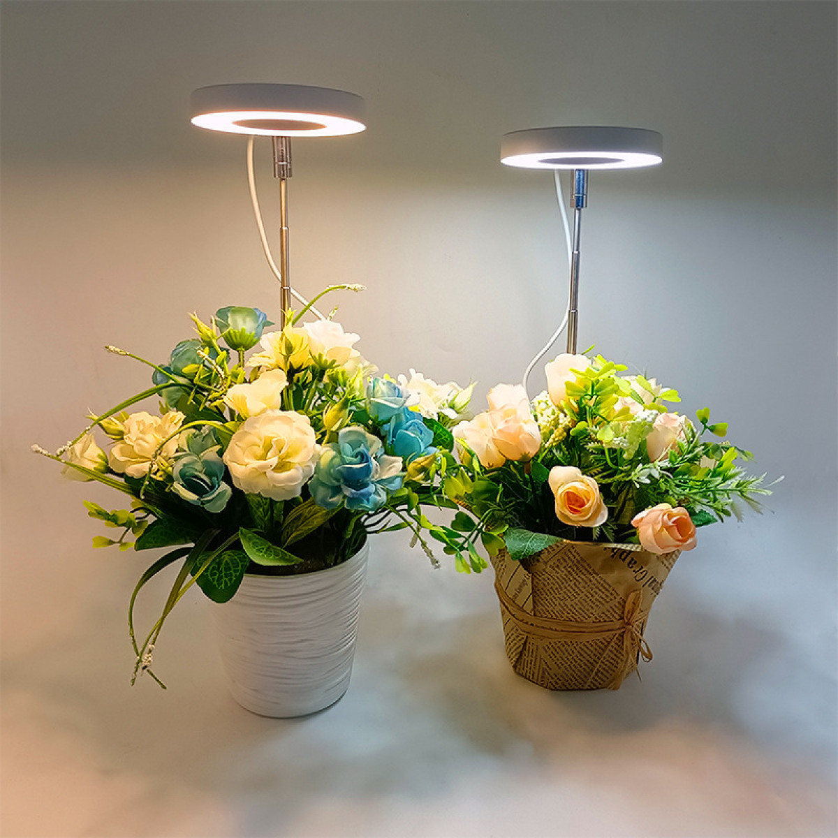 Twee bloemstukken met kleine lampjes erboven, in witte en bruine potten.