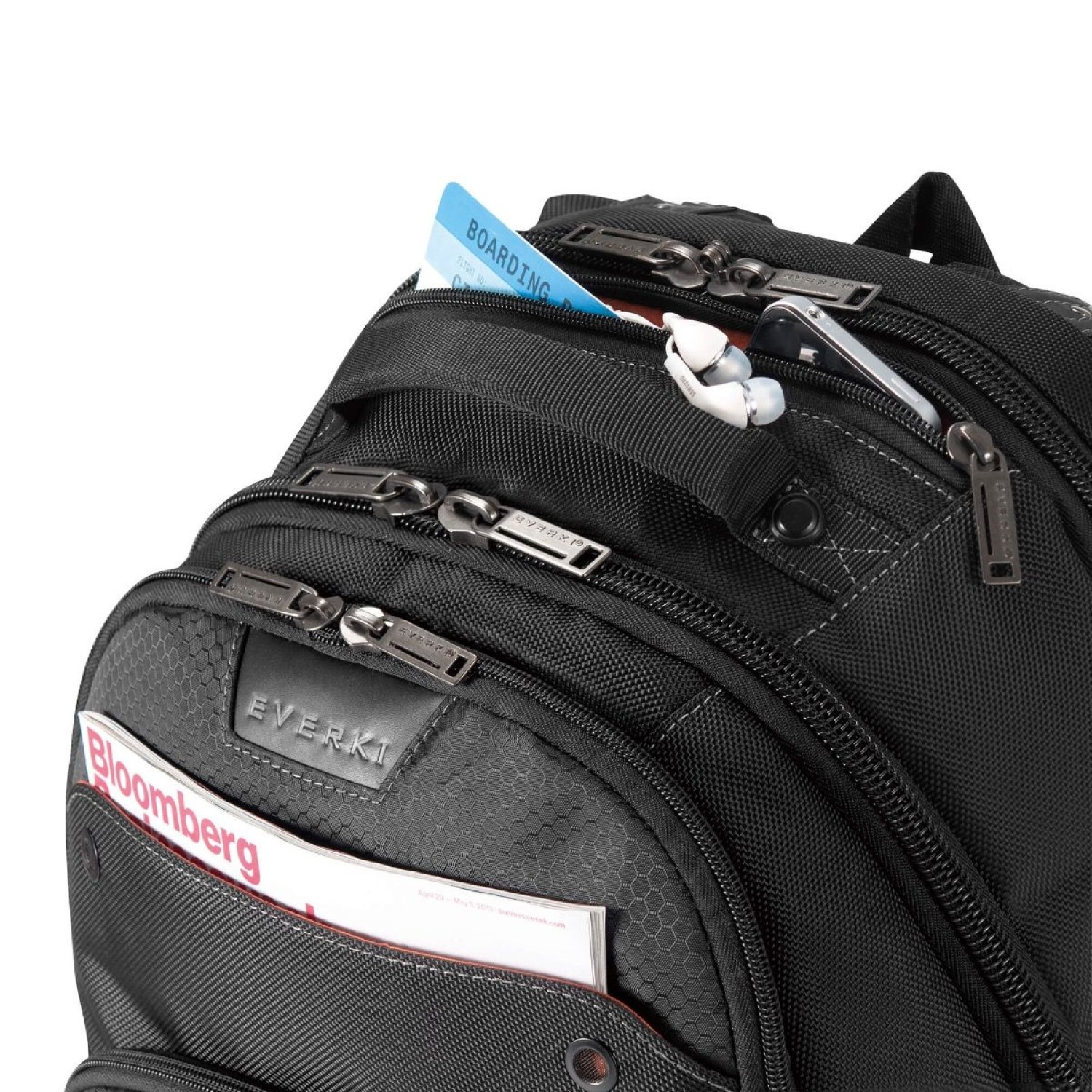 Schwarzer Rucksack mit mehreren Taschen, Reißverschlüssen und einer Bloomberg-Zeitschrift in einer Tasche.