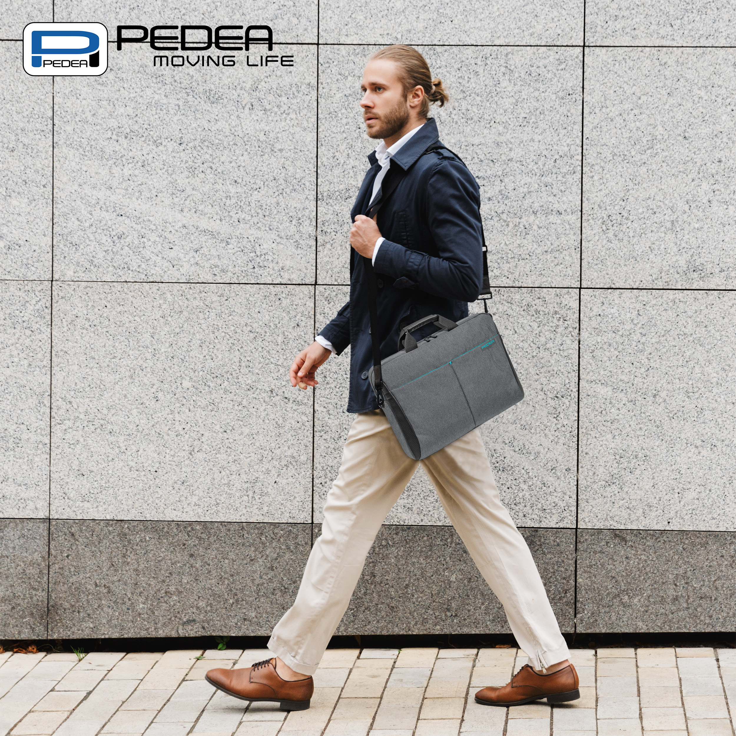 Uomo che porta una borsa per laptop grigia, cammina su un marciapiede con un muro grigio sullo sfondo.