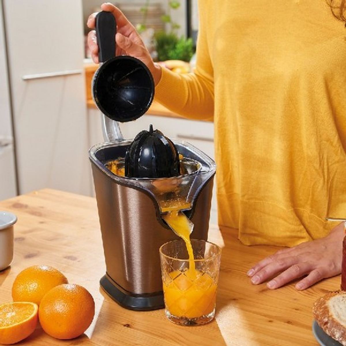 Una donna usa uno spremiagrumi. Ci sono arance e un bicchiere di succo. Lo sfondo è legno.