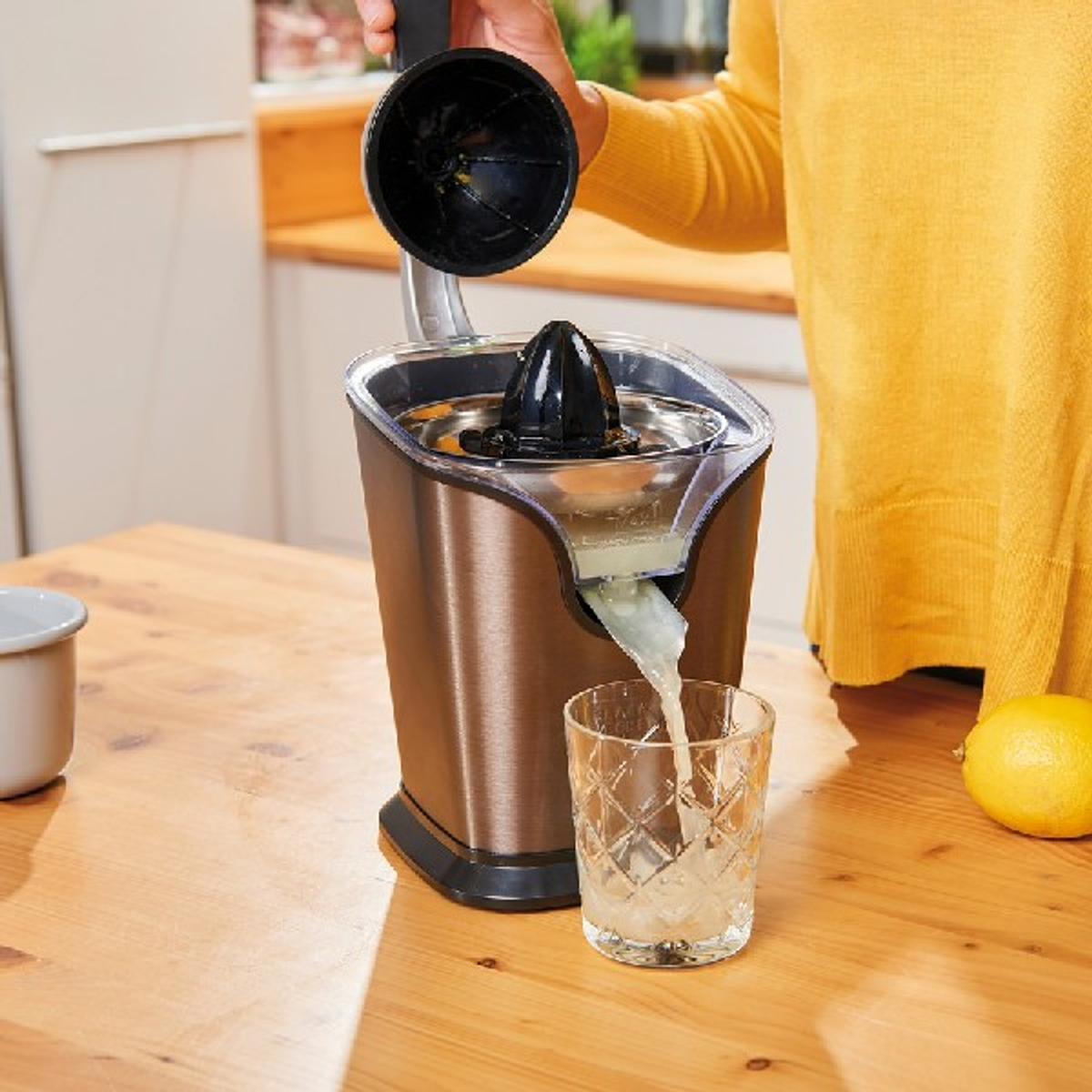 Una persona sprema succo di limone in un bicchiere con uno spremiagrumi. Ambiente cucina, luce calda.