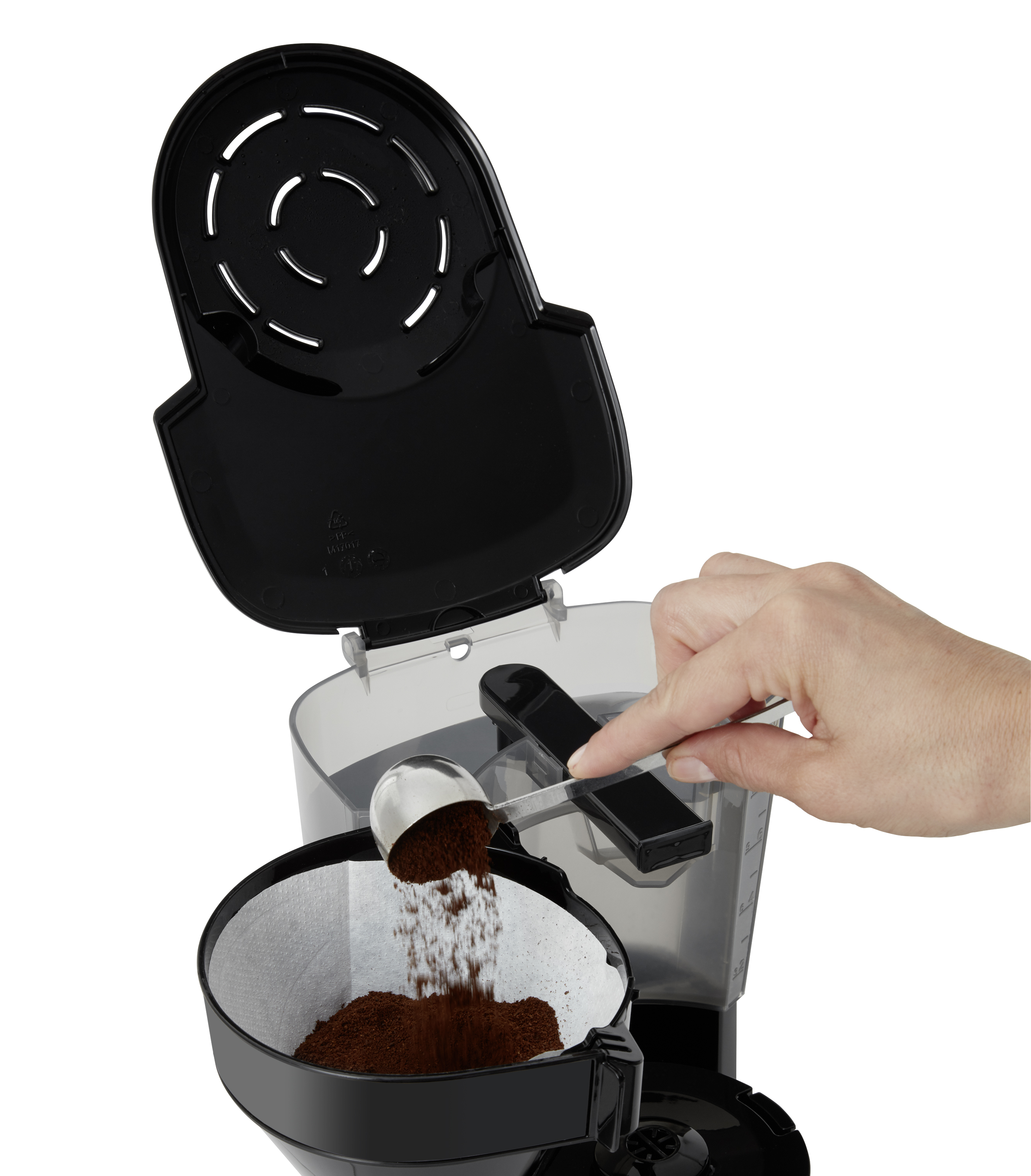 Hand gießt Kaffeepulver in einen Filter. Eine schwarze Kaffeemaschine ist im Hintergrund.