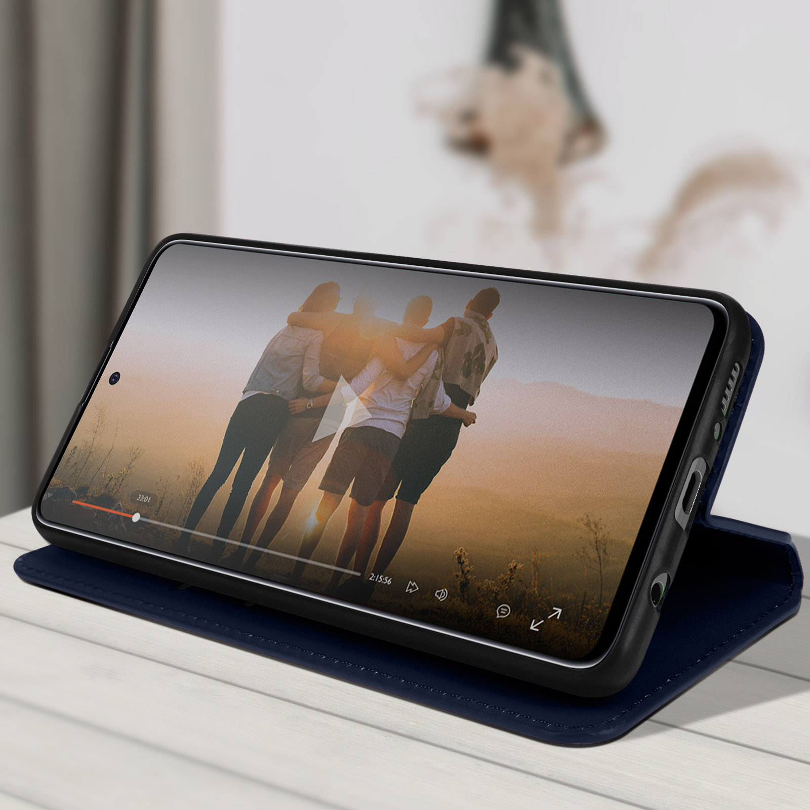 Ein Telefon in einer blauen Hülle, das ein Video auf seinem Bildschirm zeigt, auf einer Oberfläche liegend.