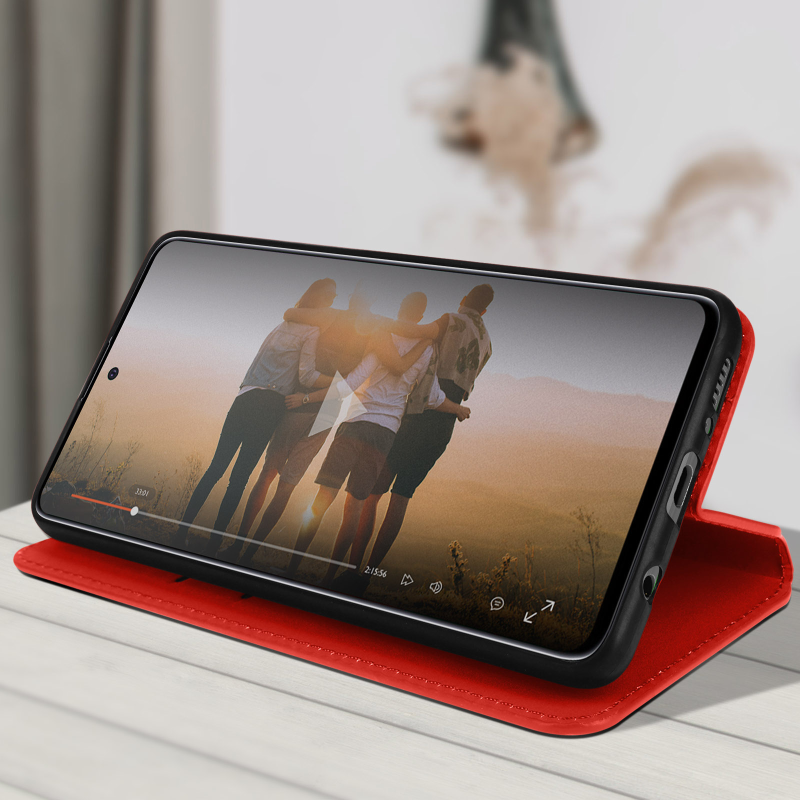 Ein Telefon in roter Hülle ist auf einem Tisch aufgestellt und spielt ein Video.