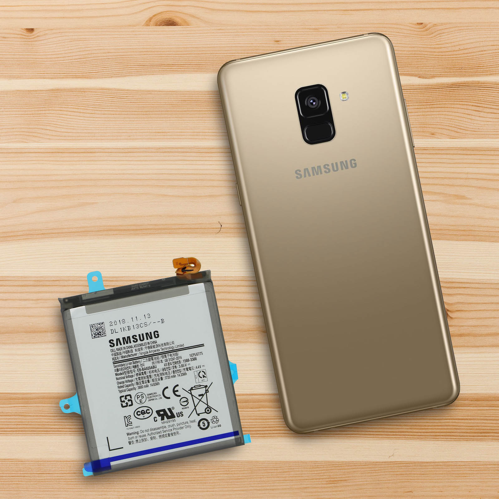 Un téléphone avec une batterie à côté, les deux sur une surface en bois.