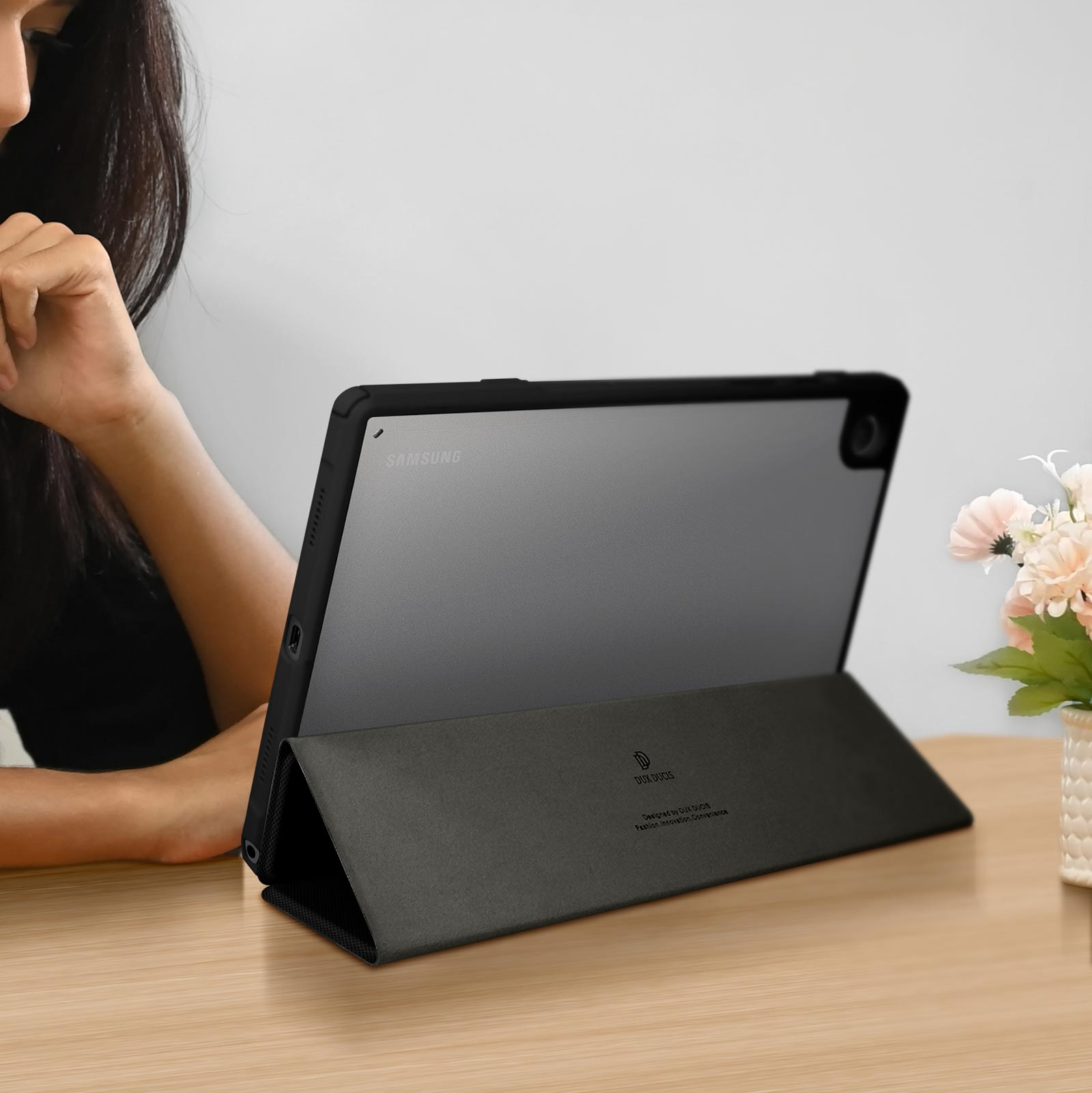 Una donna accanto a un tablet in una custodia su un tavolo di legno. Fiori sullo sfondo.