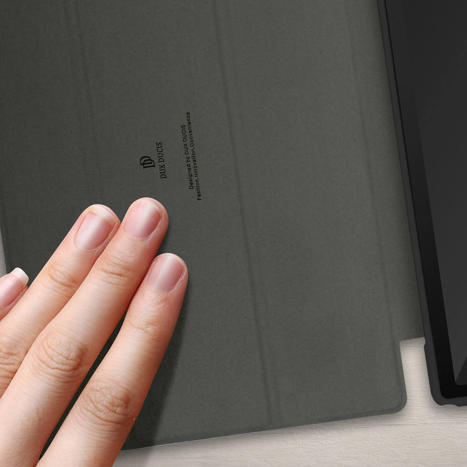Mano che tocca una cover grigia per tablet, con testo: 'Designed by Dux Ducis'.