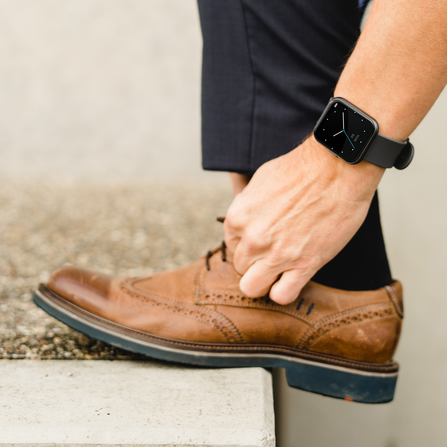 Die Hand einer Person bindet einen Schuh. Die Person trägt eine Smartwatch und steht auf Treppen.