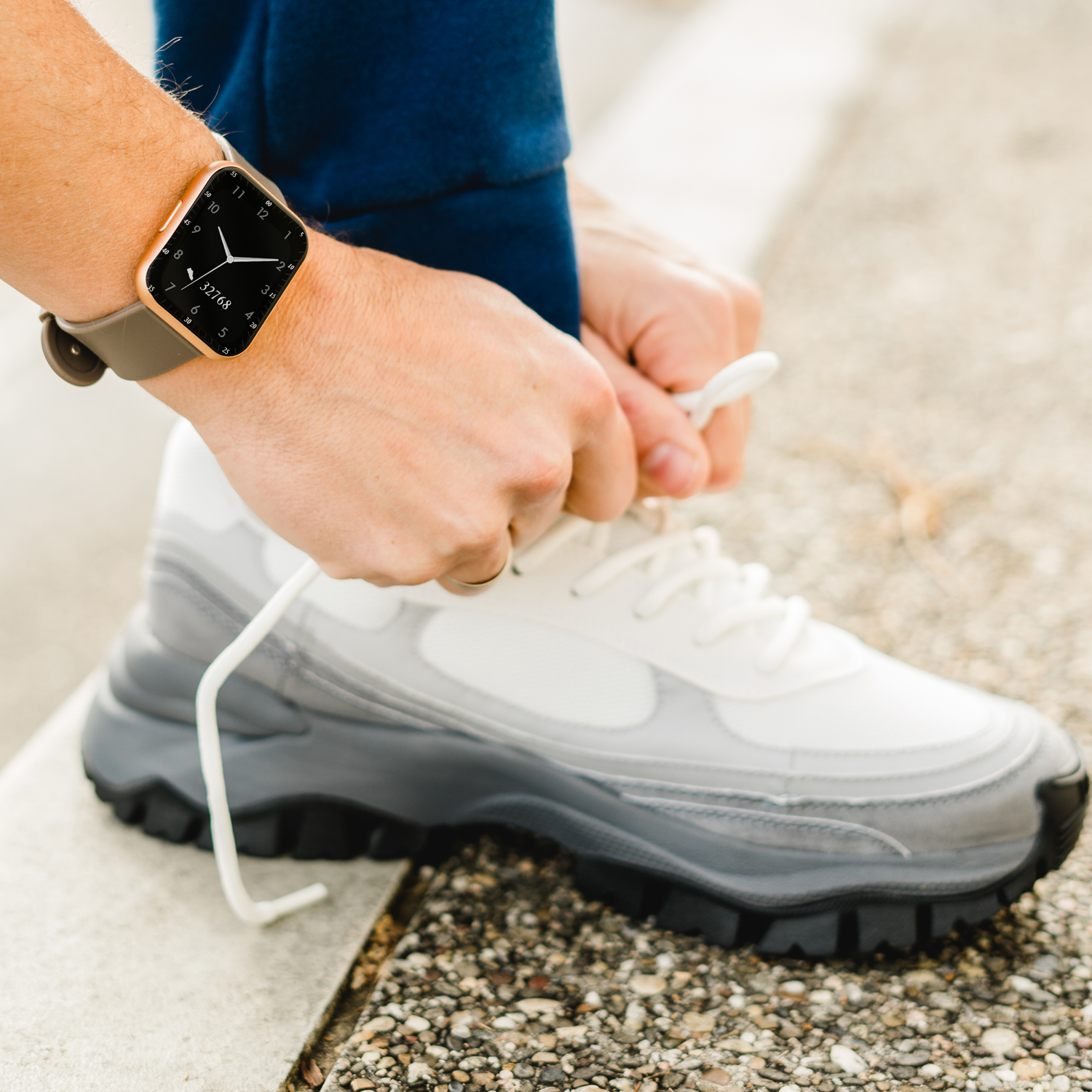 Osoba wiąże but sportowy, nosząc smartwatch na nadgarstku, na szarej powierzchni.