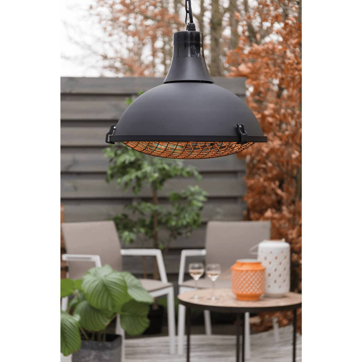 Schwarze Hängelampe für den Außenbereich. Darunter ein Metallgitter. In einem Garten mit Stühlen und Pflanzen.
