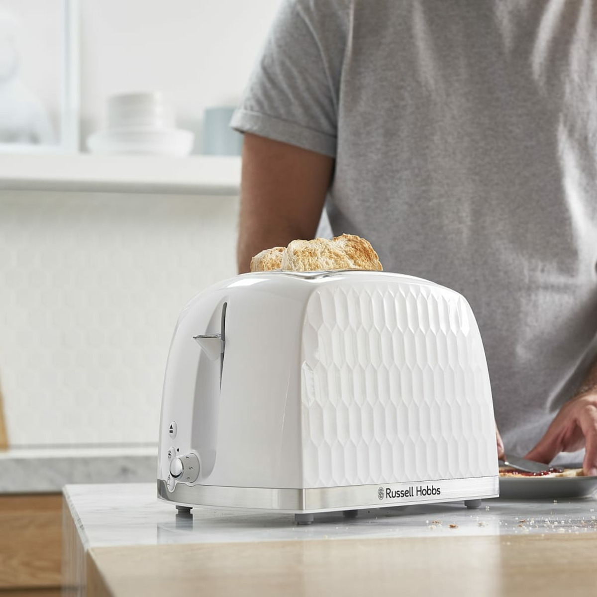 Biały toster z kromkami chleba na wierzchu, osoba w szarej koszuli przygotowuje kromki.