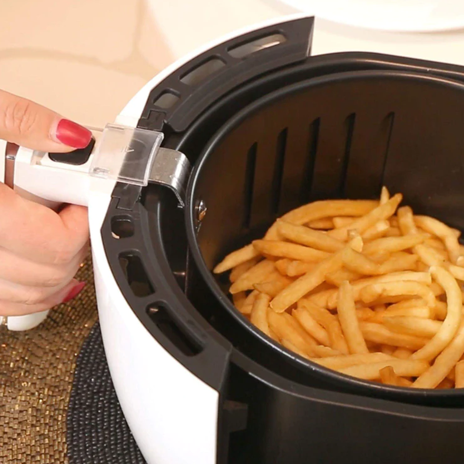 Eine Heißluftfritteuse mit Pommes Frites und eine Hand, die den Griff hält.