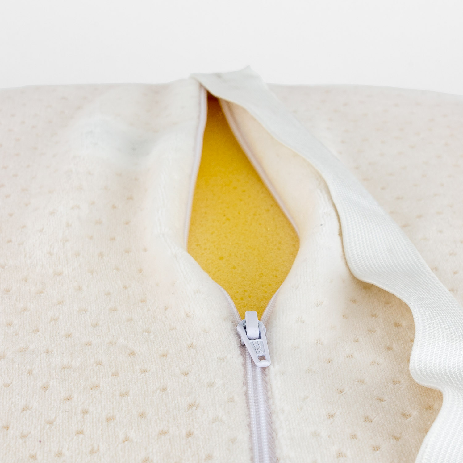 Primer plano de almohada blanca con cremallera abierta, revelando relleno de espuma amarilla.