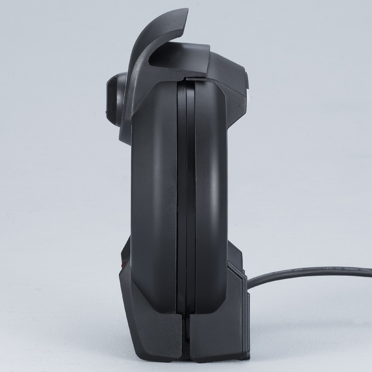 Czarny kontroler do gier jest pokazany z boku, podłączony do gniazdka ściennego.