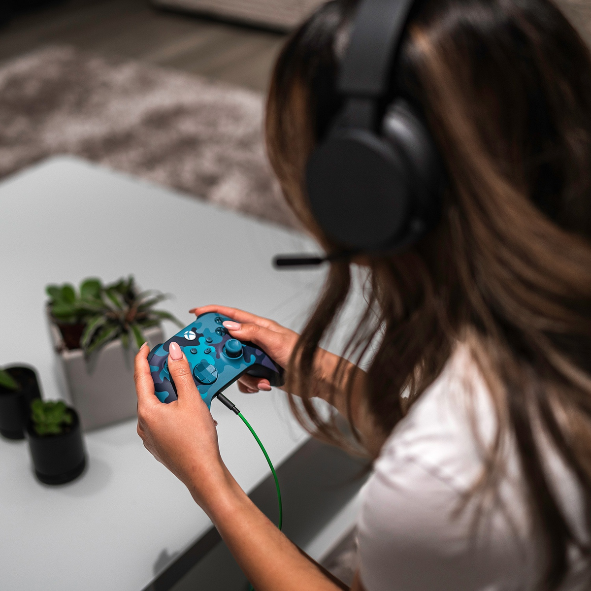 Person hält blauen und tealfarbenen Gamecontroller. Sie trägt Kopfhörer und spielt ein Spiel.