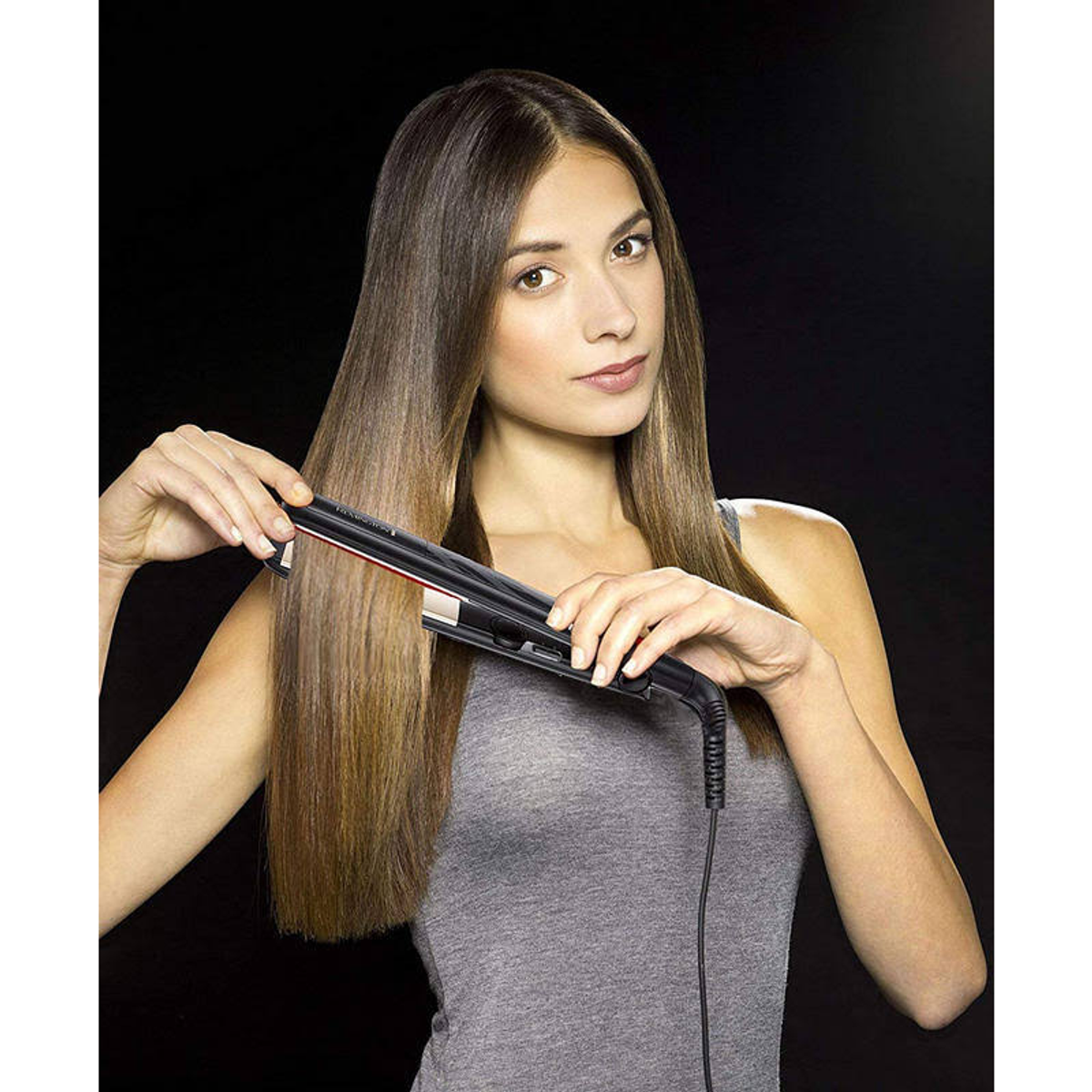 Mujer con pelo liso usando plancha, fondo negro.
