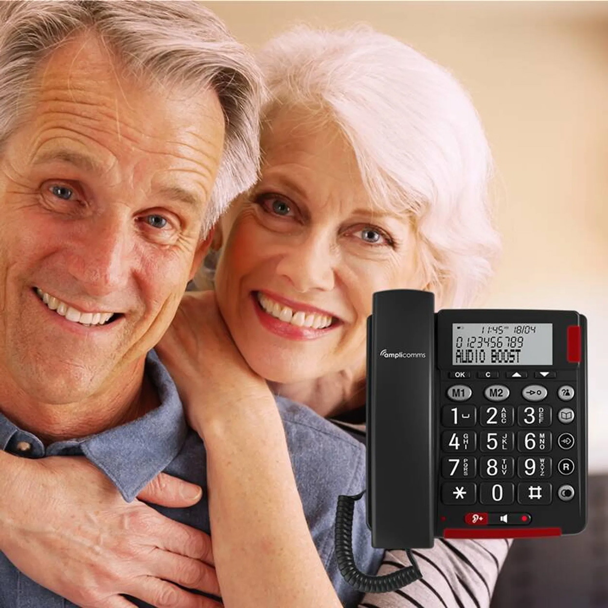 Una coppia anziana sorridente, la donna che abbraccia l'uomo, con un telefono nero con pulsanti grandi di fronte.