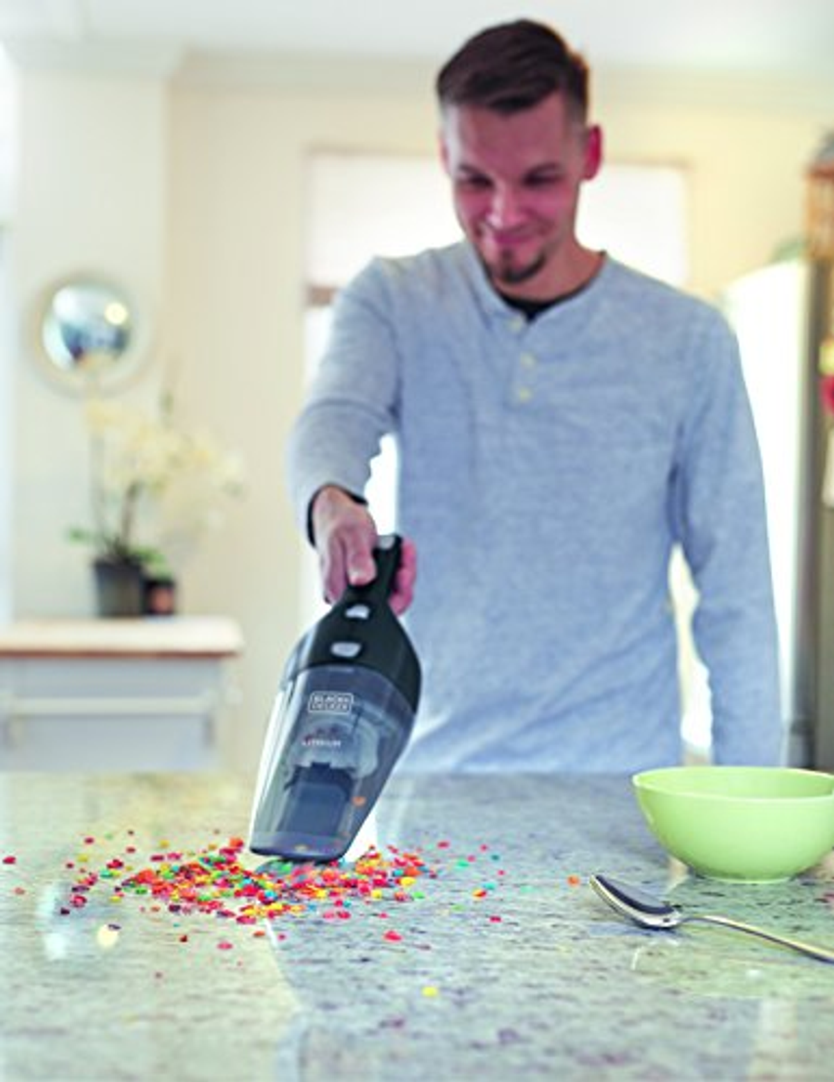 Uomo che aspira cereali colorati rovesciati da un piano di lavoro con un aspirapolvere a mano.