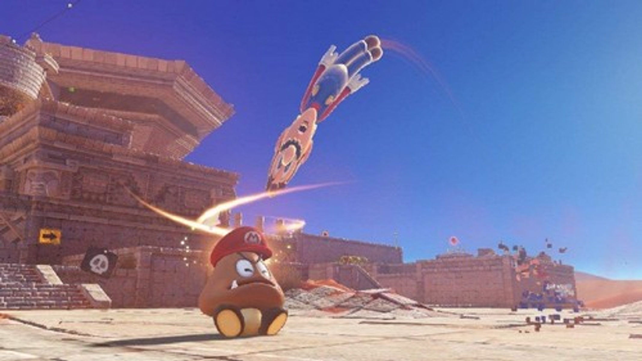Mario skacze w stronę Goomby w pustynnym krajobrazie ze starożytnymi strukturami.