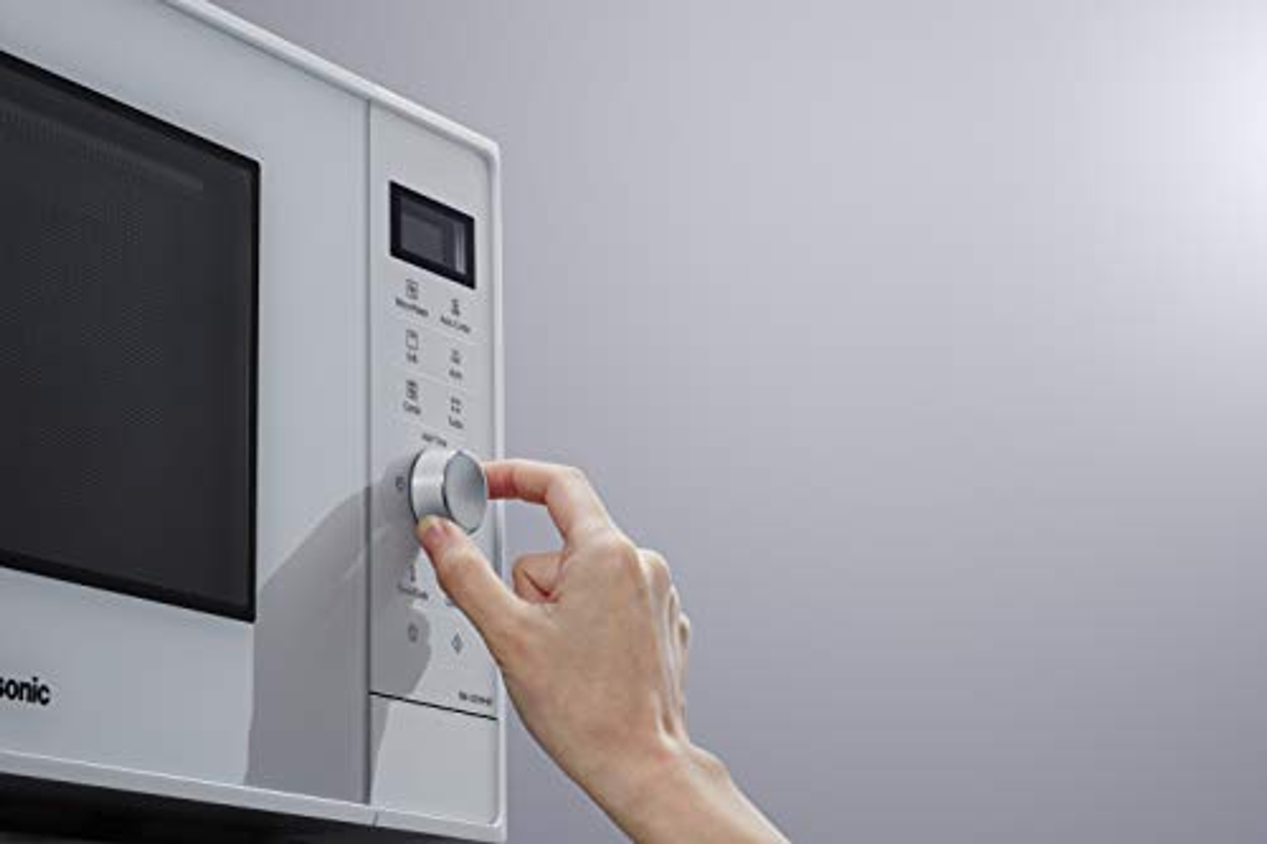 Ręka regulująca pokrętło białej kuchenki mikrofalowej. Kuchenka mikrofalowa ma cyfrowy wyświetlacz i przyciski.