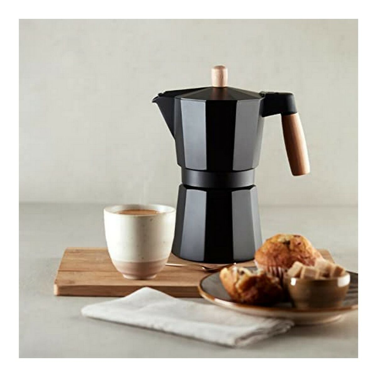Schwarzer Kaffeekocher mit Tasse, Muffins und Teller. Holzbrett.