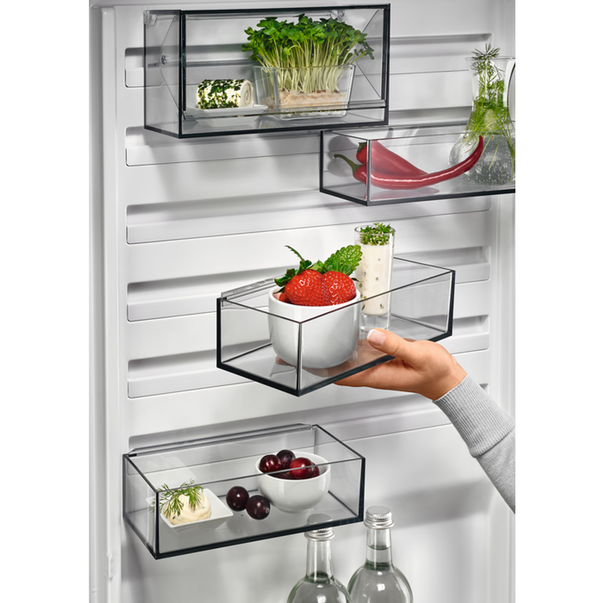 Interior de refrigerador con comida en recipientes de vidrio. Mano entrando.