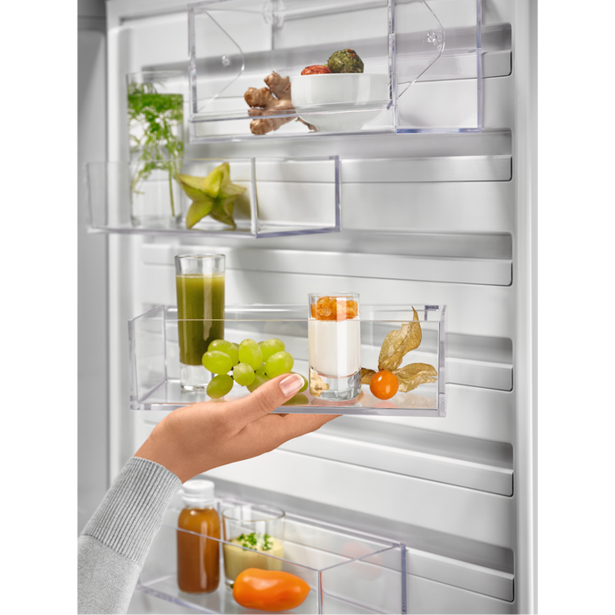Mano sosteniendo estantes transparentes con alimentos en el refrigerador.