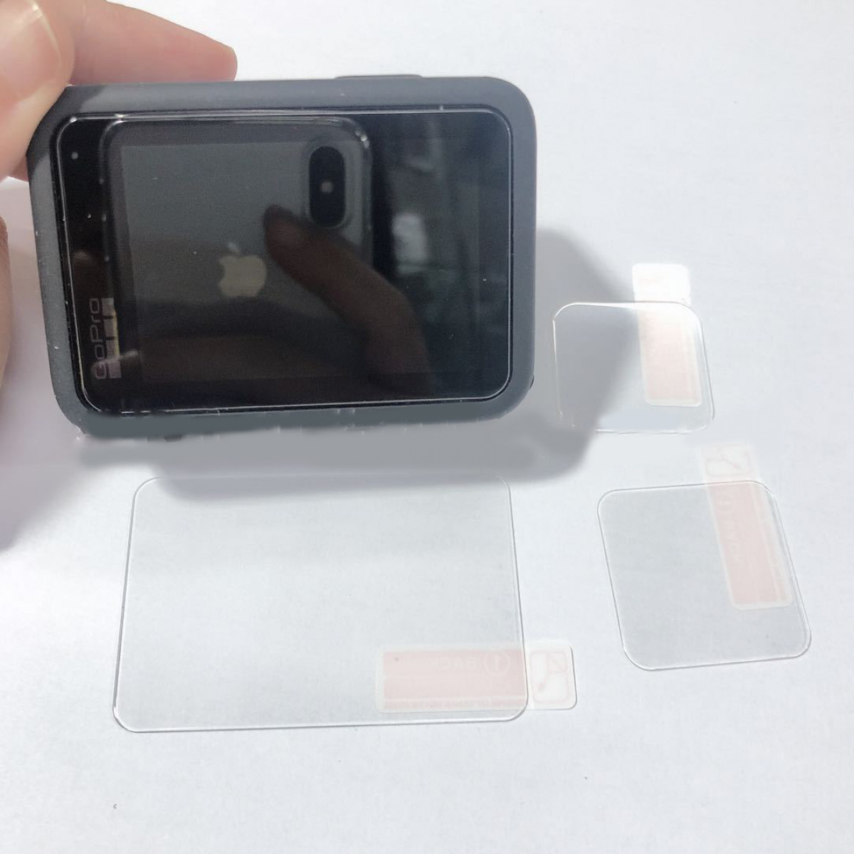 Una cámara de acción GoPro y protectores de pantalla sobre una superficie blanca.