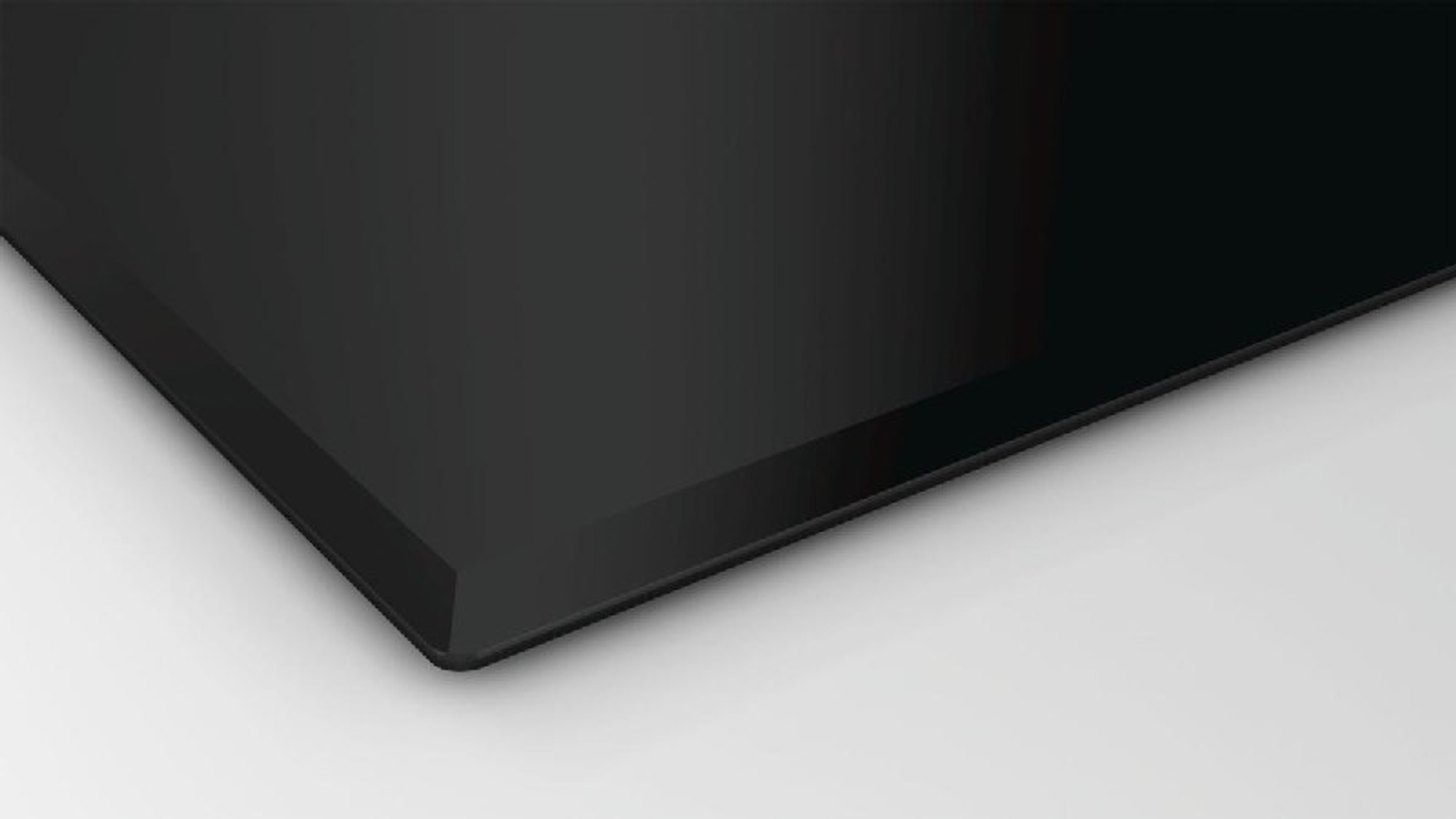 Esquina de placa de inducción negra con fondo blanco.